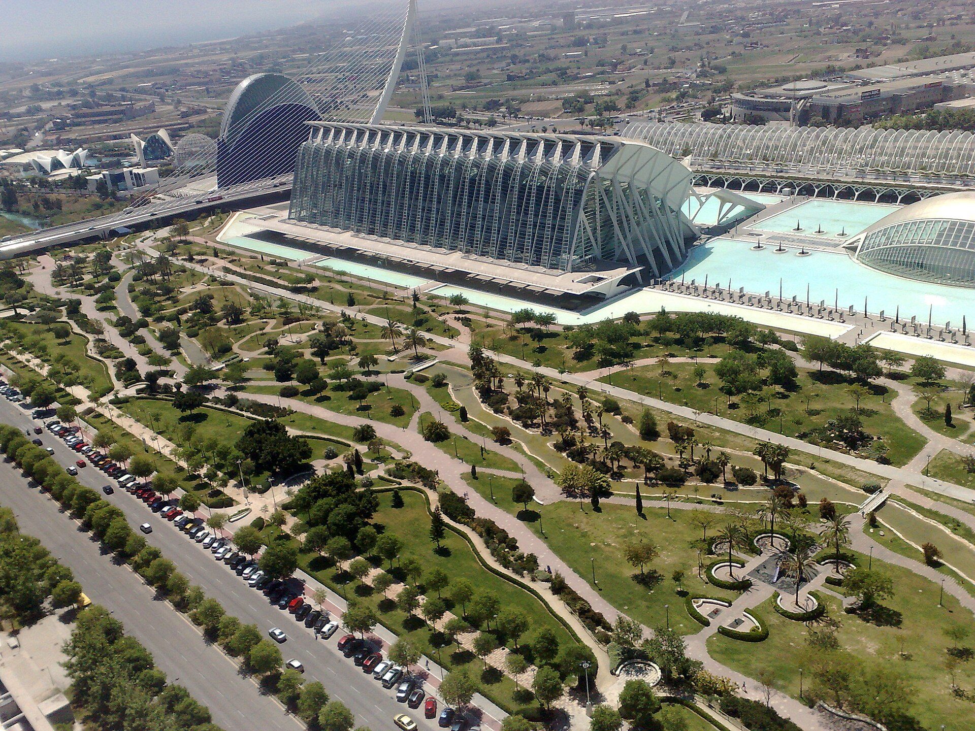 Aerial view of a modern hotel with a large pool, green gardens, and a distinctive curved roof.