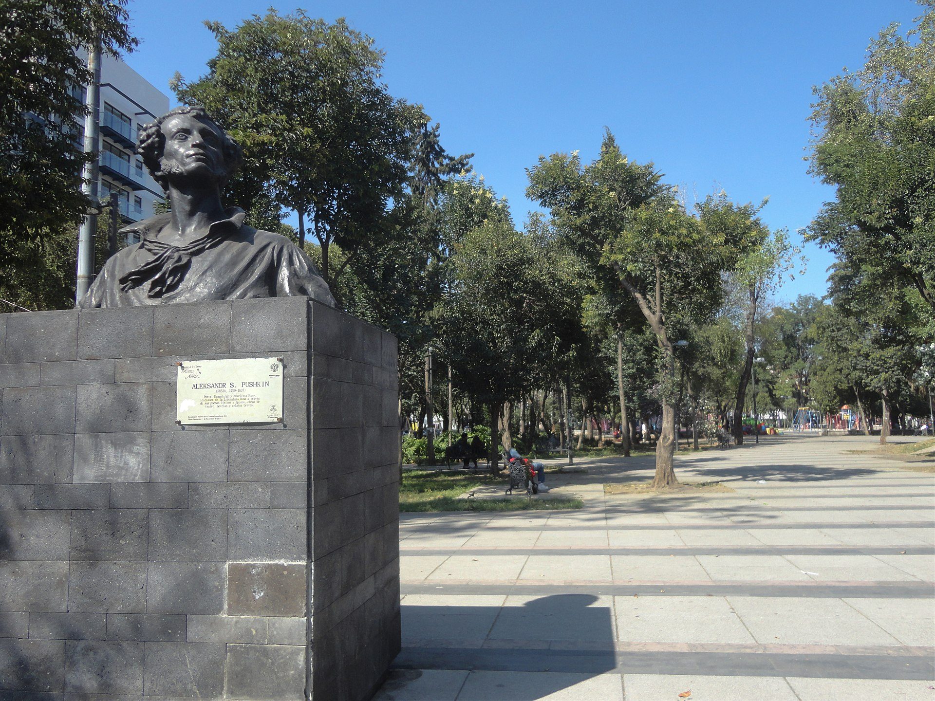 Alt text: Outdoor bronze bust statue in a park with trees and a clear blue sky.