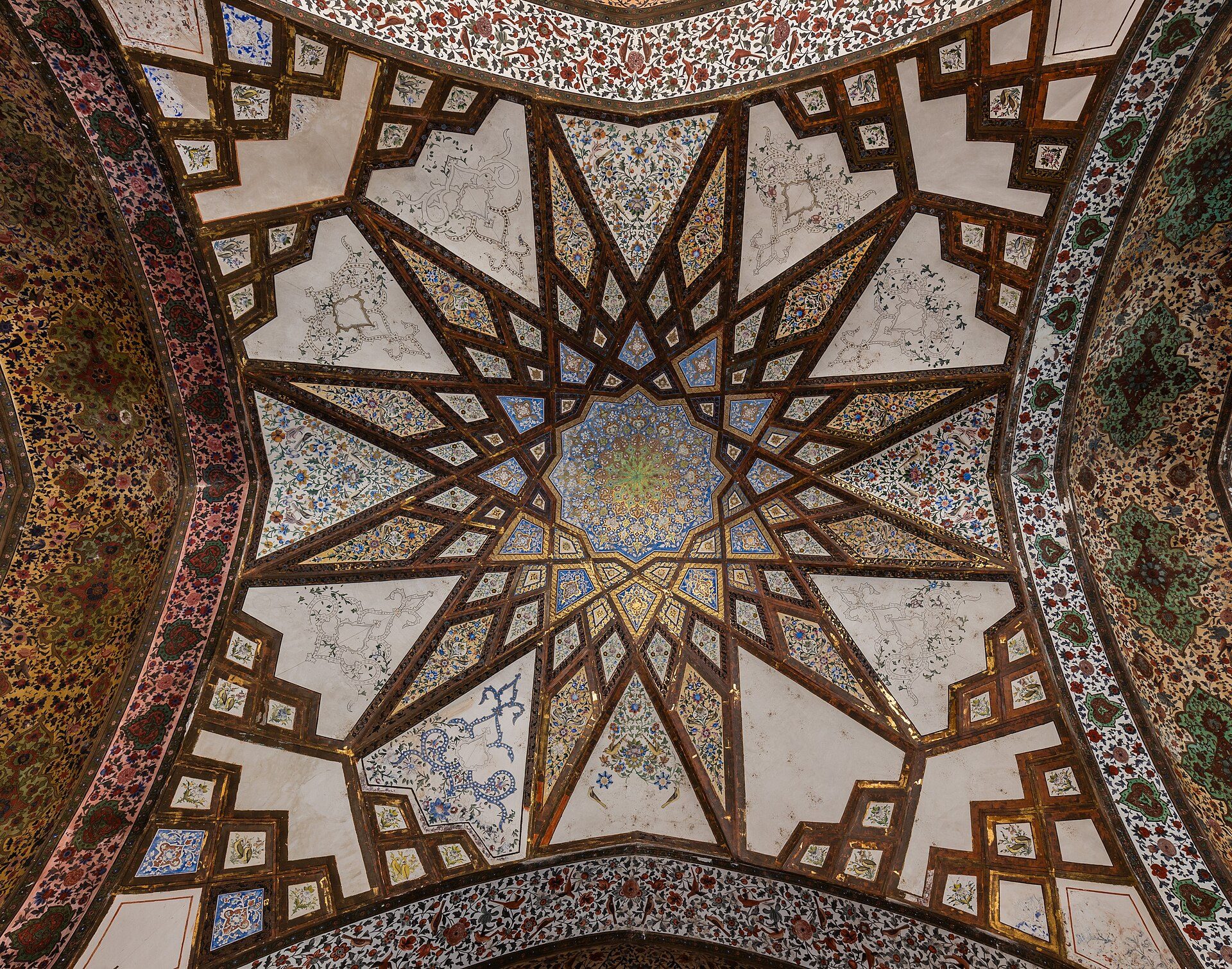 Intricate ceiling with star-shaped patterns and colorful geometric designs in a room.