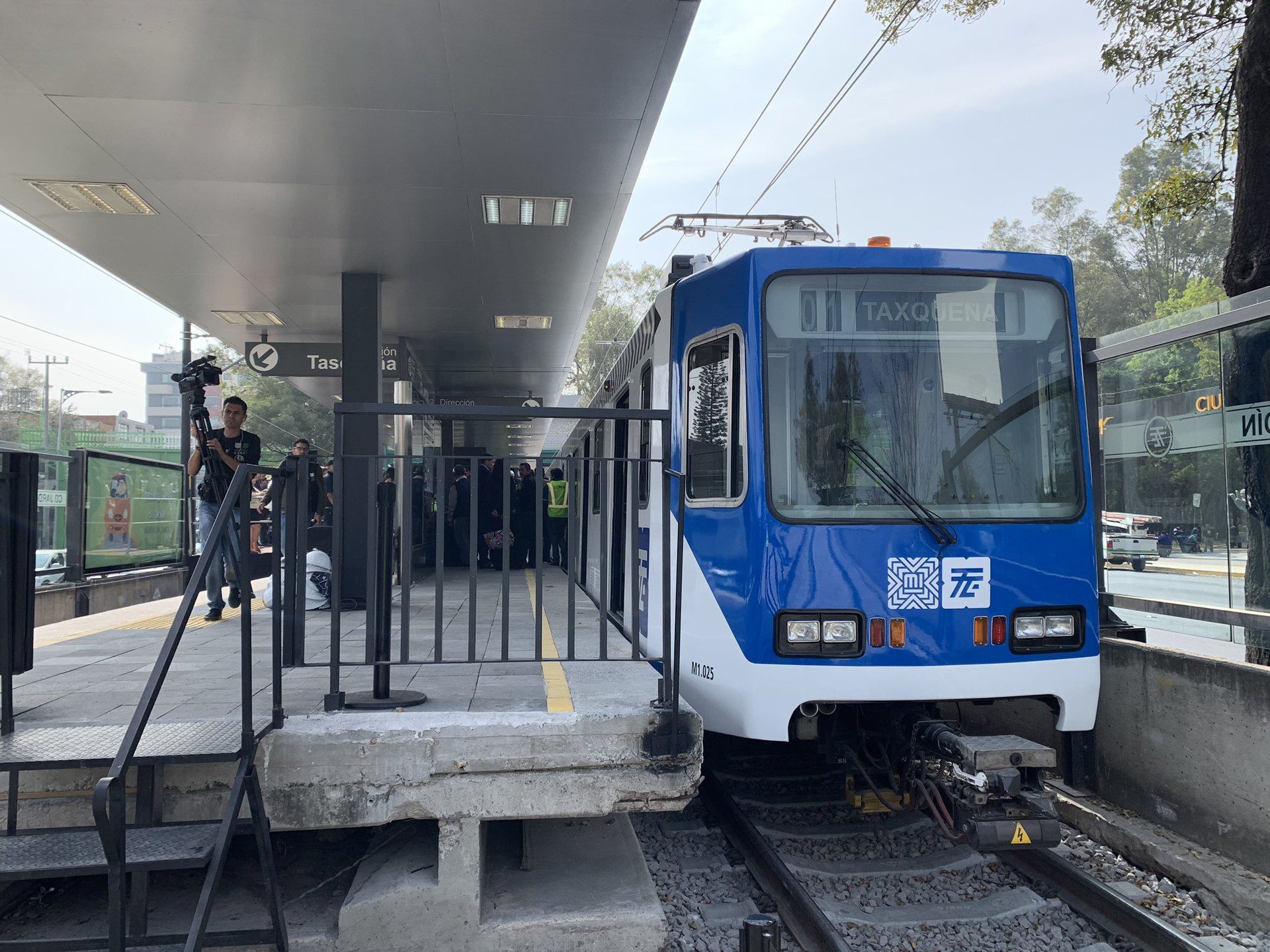 Alt text: Blue and white train at station platform with passengers and overhead shelter.