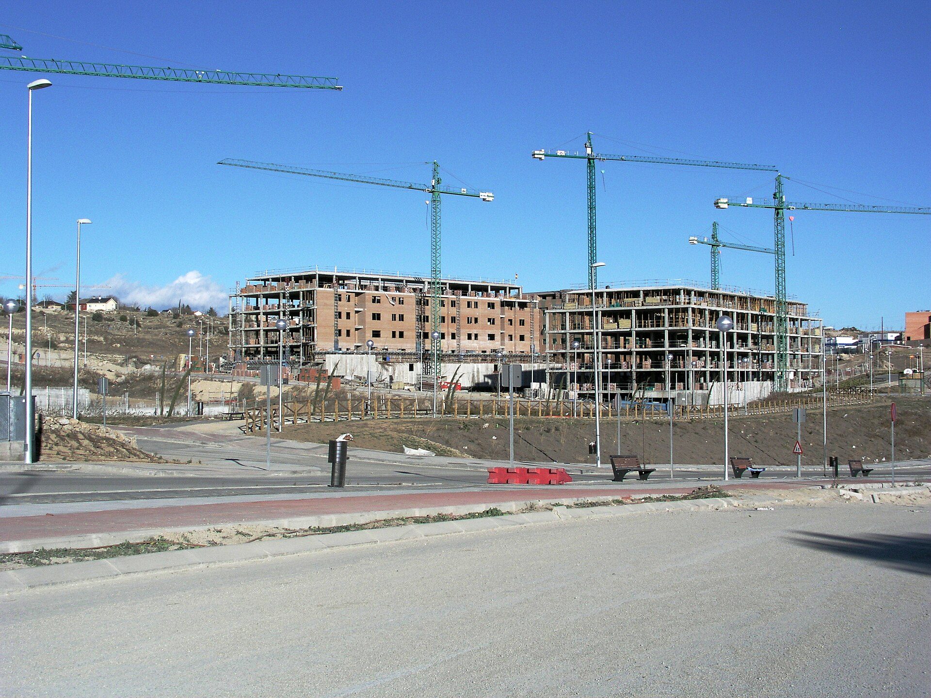 Construction site with multiple cranes and unfinished buildings under a clear blue sky.
