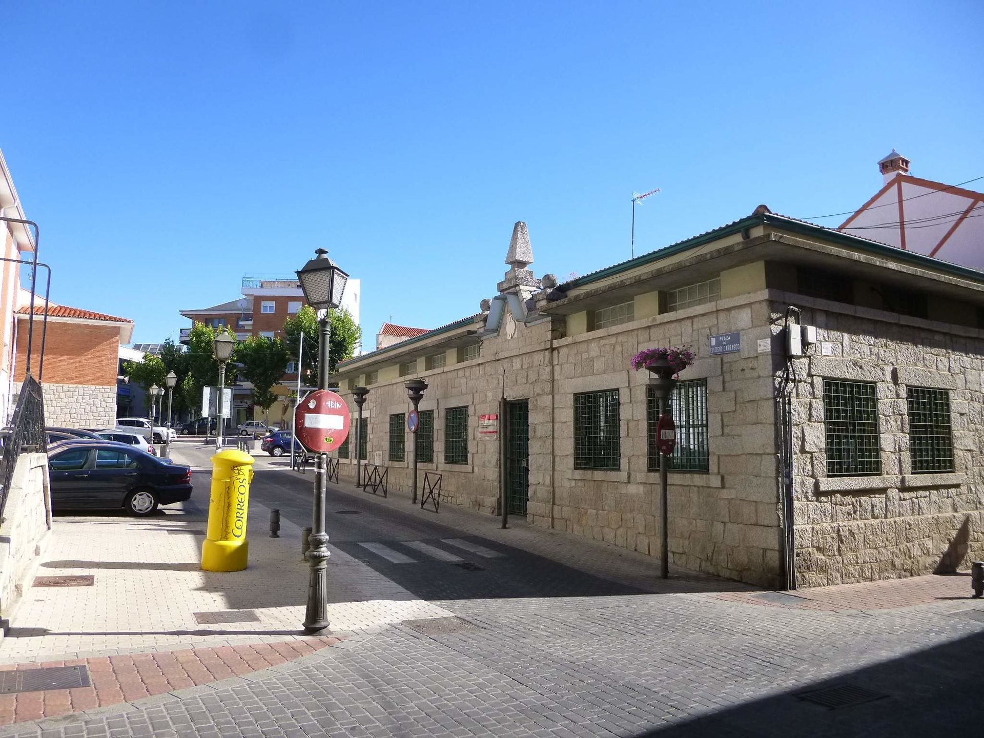 A stone building with green shutters, a small garden, and a clear blue sky.