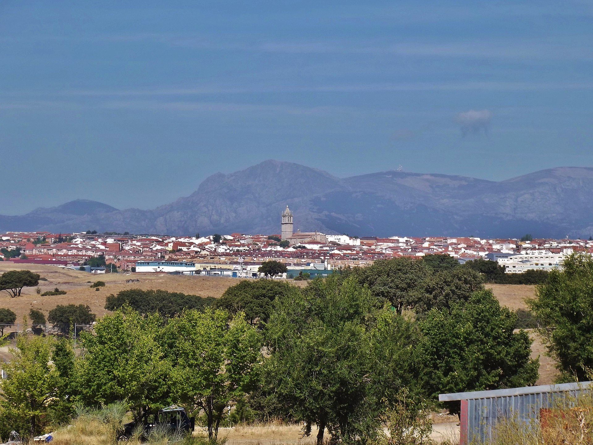 Alt text: Panoramic view of a town with a church tower, surrounded by mountains and greenery.