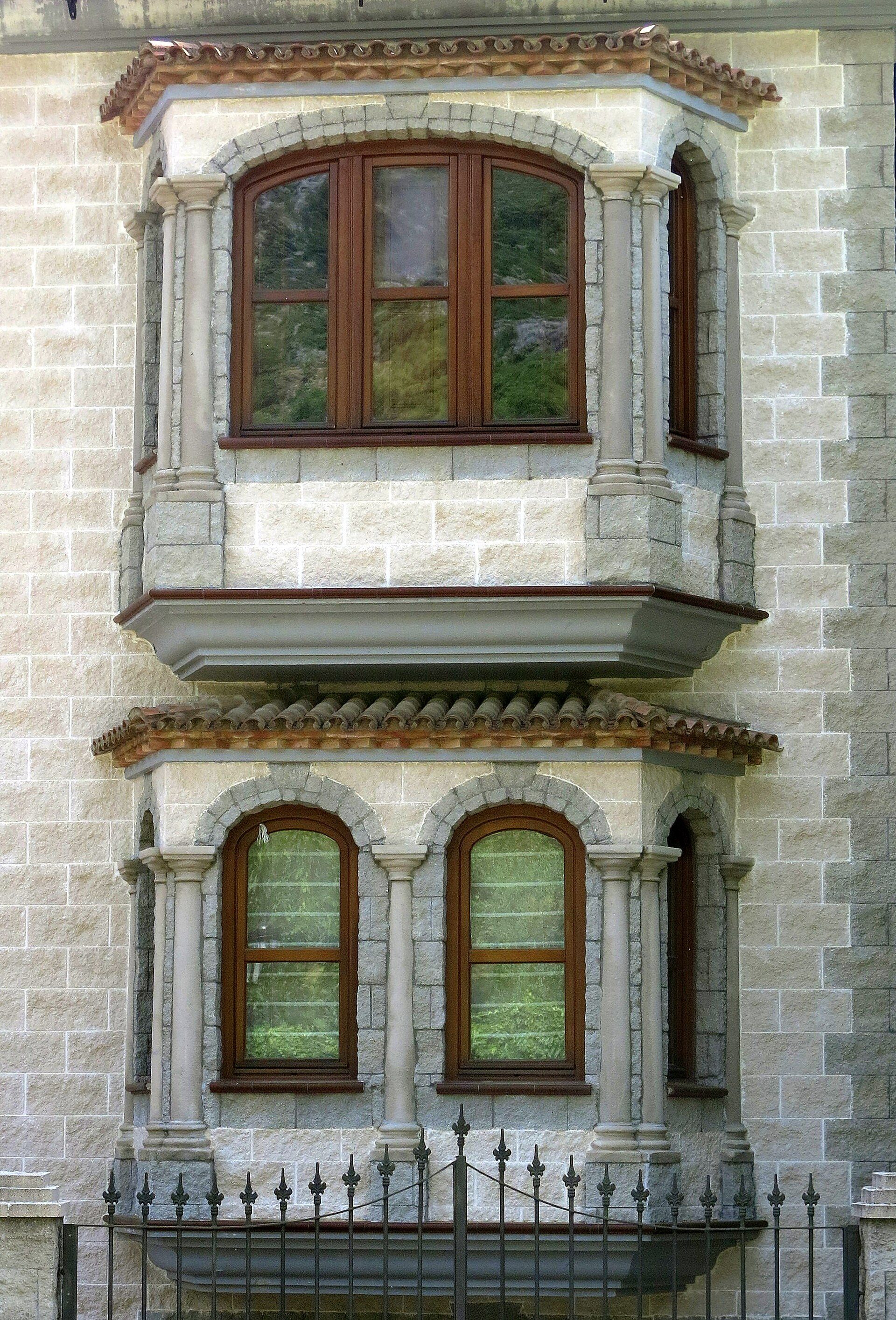Alt text: Bay window with wooden frame, stone facade, and decorative columns.