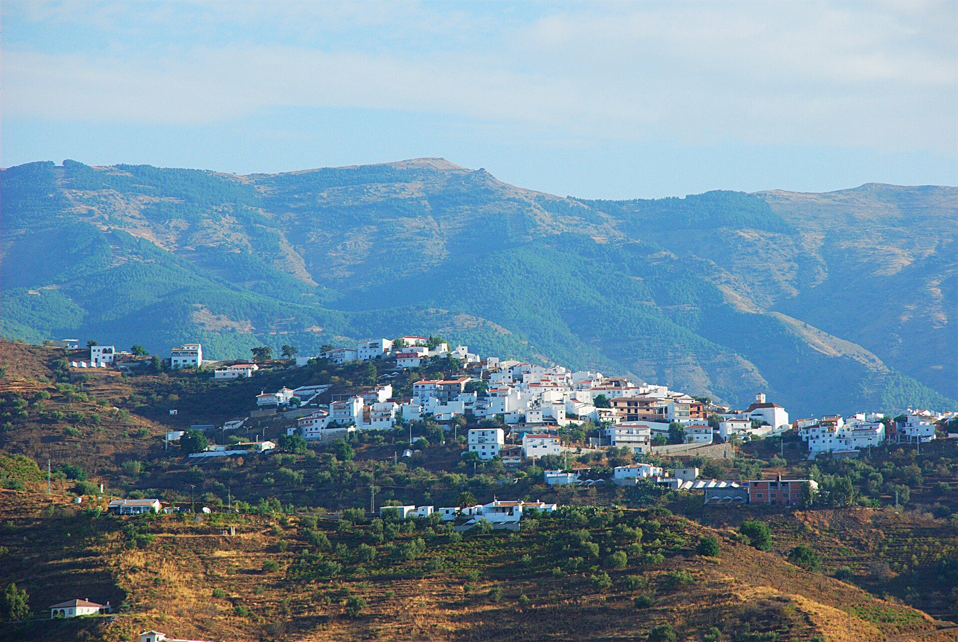 Alt text: White-walled house with mountain view, featuring a spacious living room and balcony.
