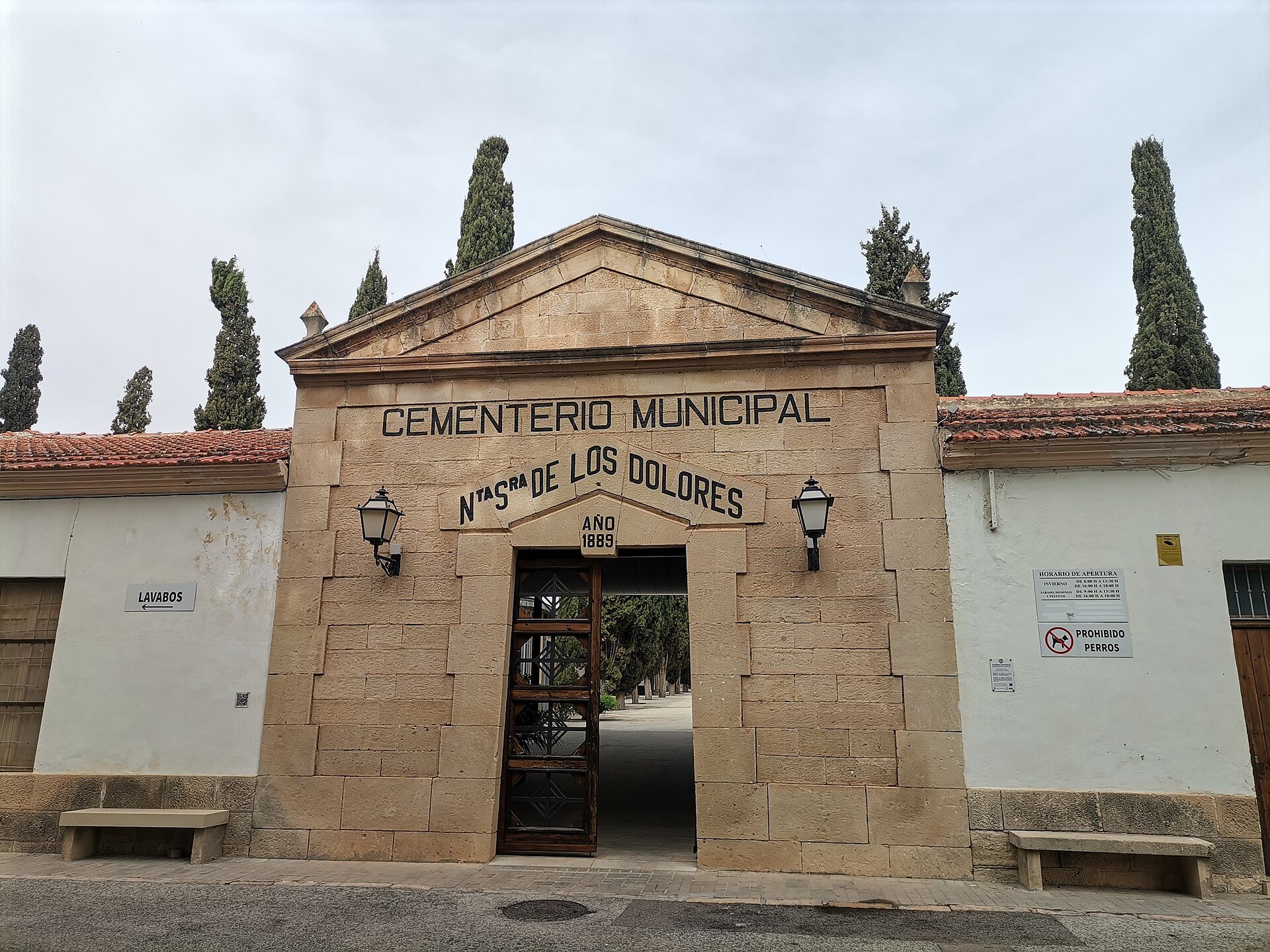 Alt text: Stone archway entrance to a cemetery with tall trees and a clear sky.
