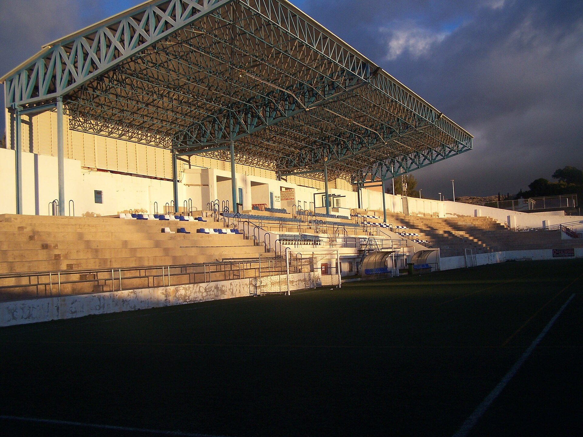 Empty stadium with seating, large roof, and open field.