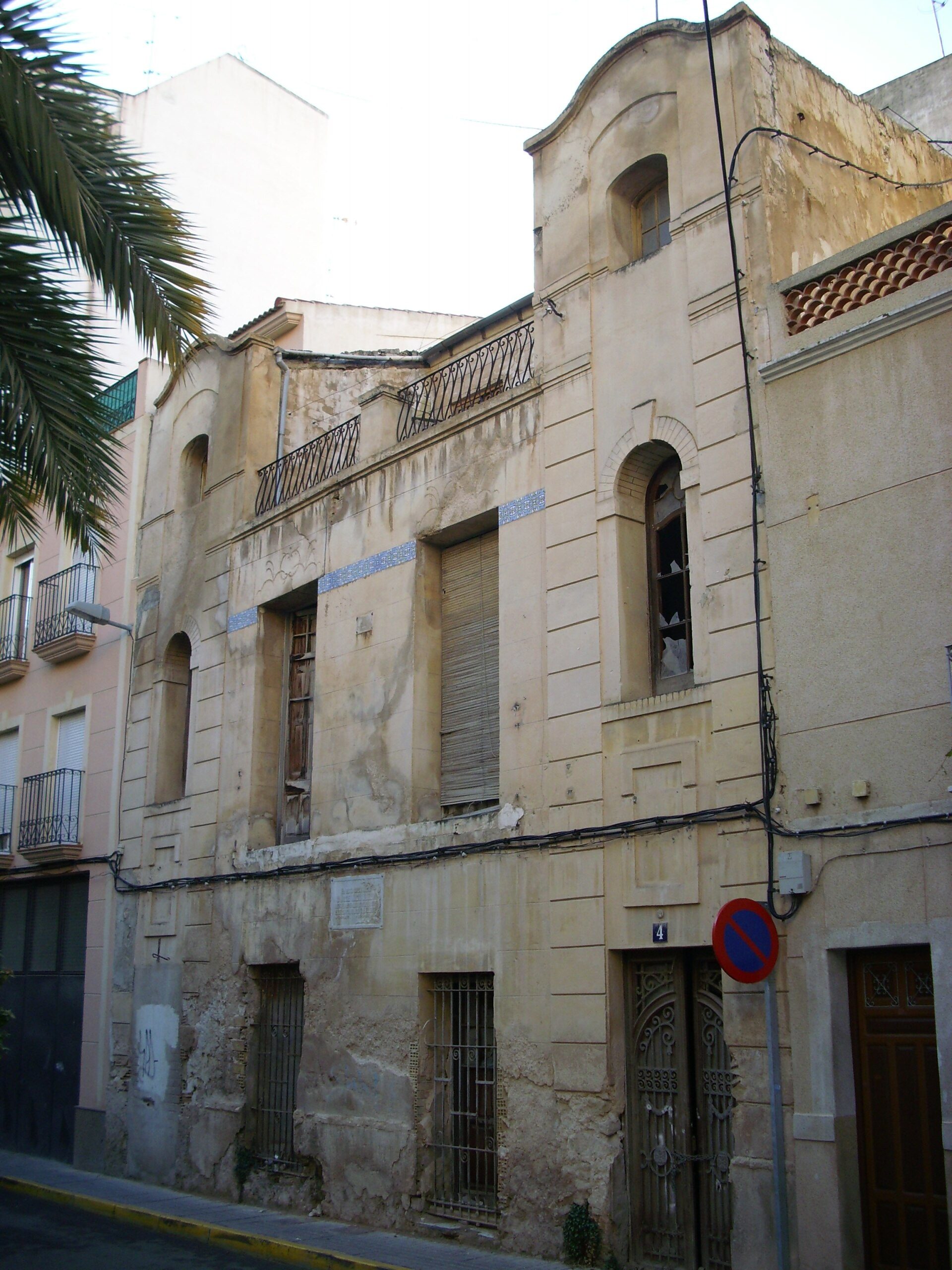 Old building with arched windows, balconies, and a view of palm trees.