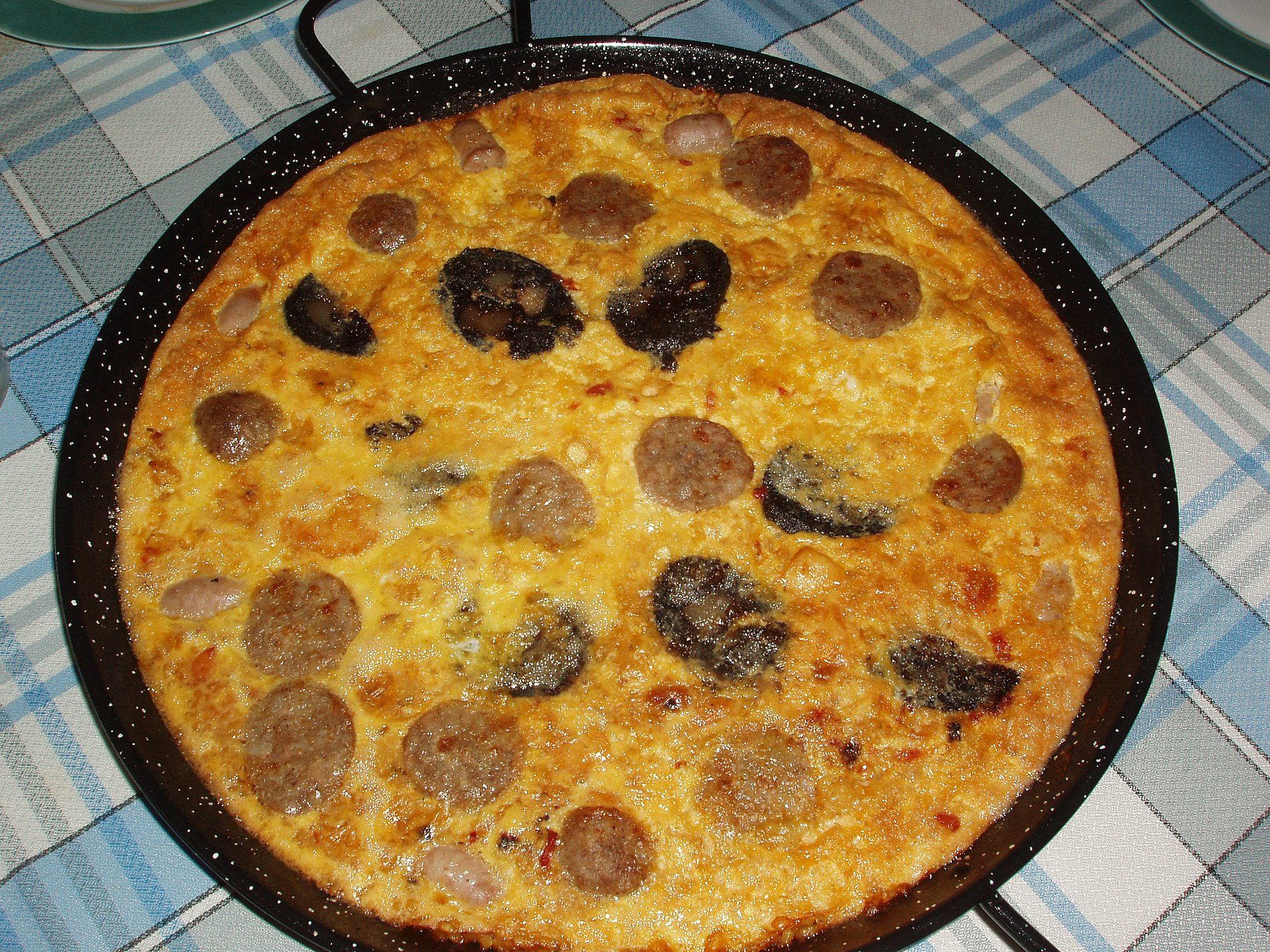 A pan of sausage and mushroom pizza on a checkered tablecloth.