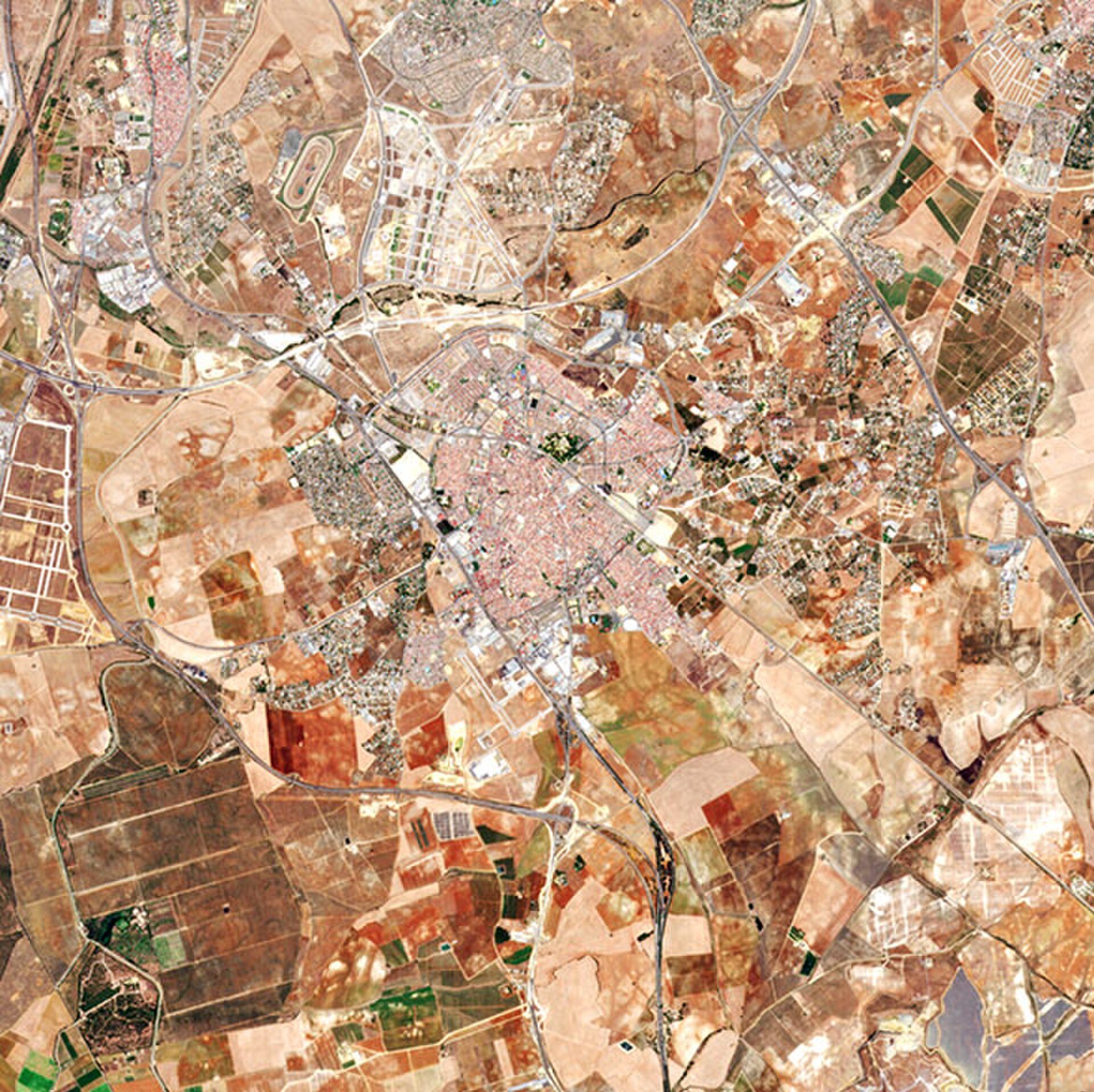 Aerial view of a city with various buildings, roads, and agricultural fields.