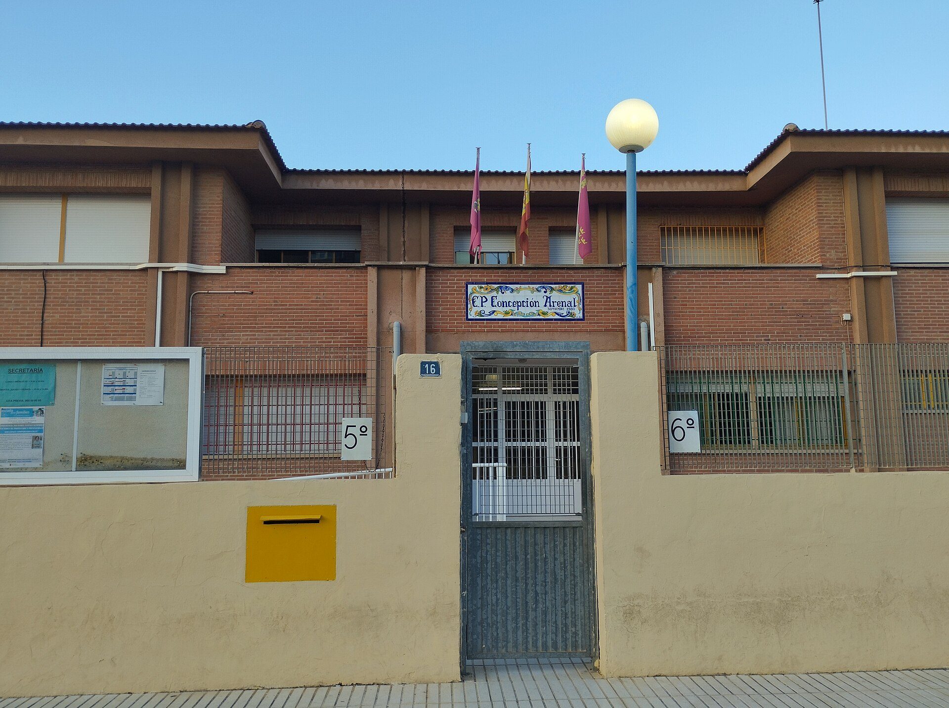 Alt text: "Brick building with sign 'CP Girona Rambla', flags, and a yellow mailbox.
