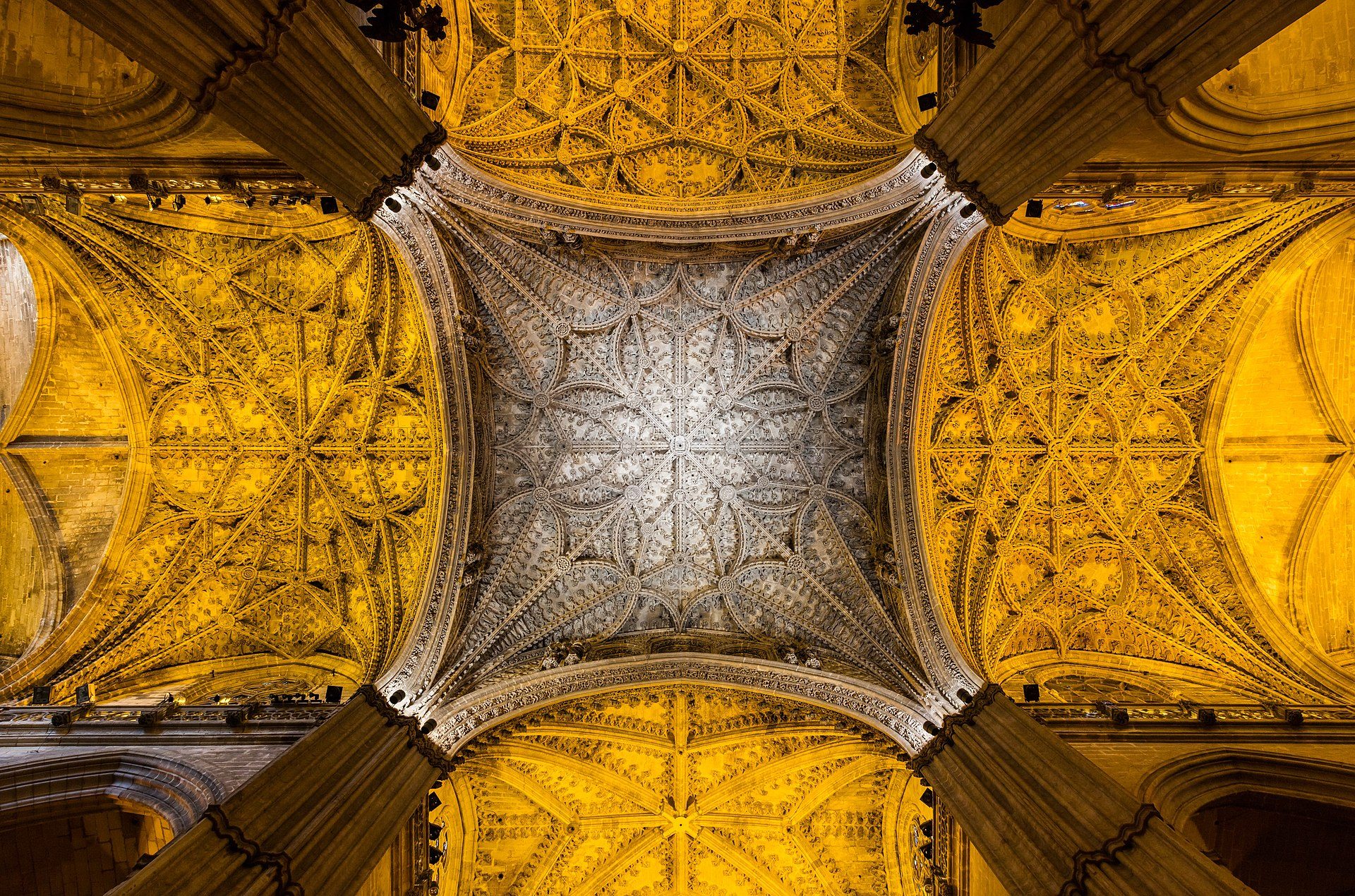 Intricate vaulted ceiling with ornate patterns and golden hues in a grand hall.