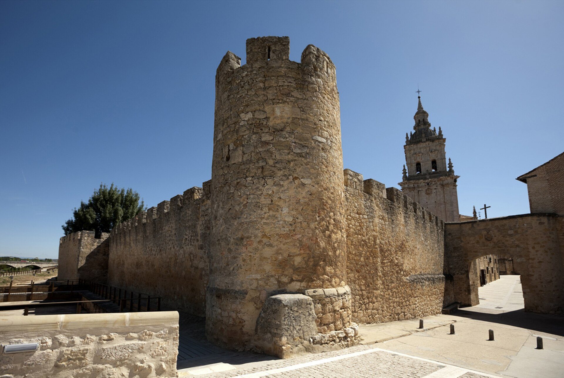 A medieval stone tower with a clear blue sky and a church in the background.
