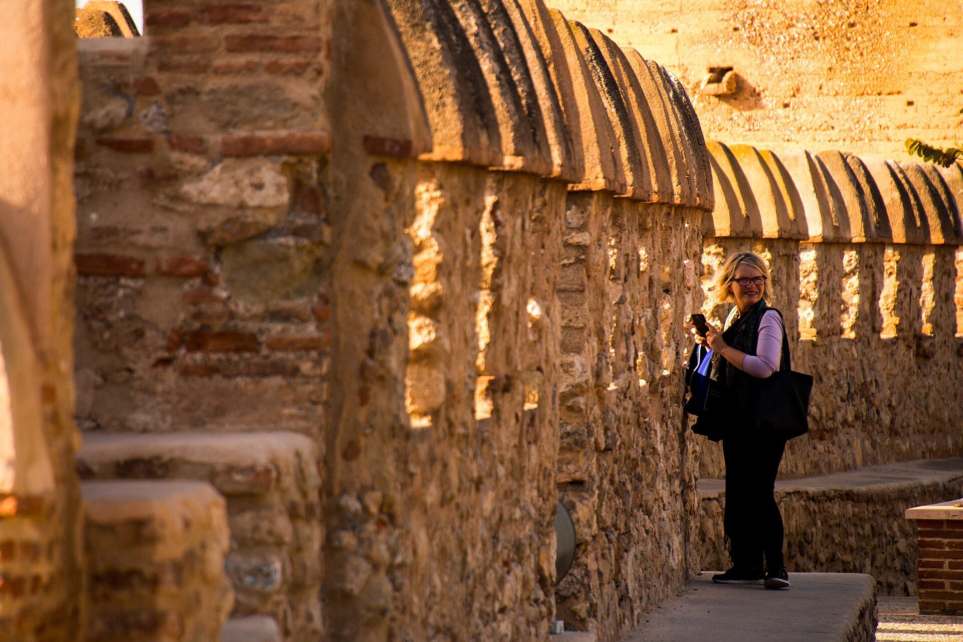 A woman stands in front of a historic stone wall with arched windows, capturing the view.