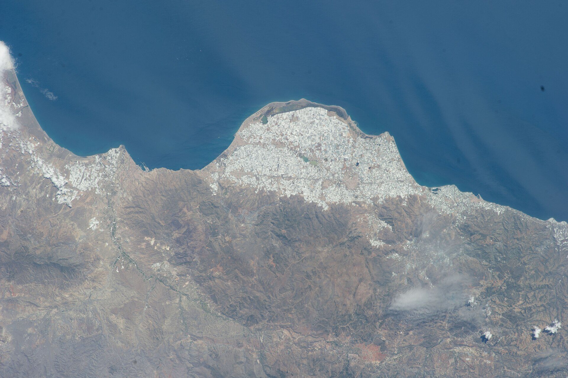 Aerial view of a coastal city with a mountainous backdrop and ocean view.
