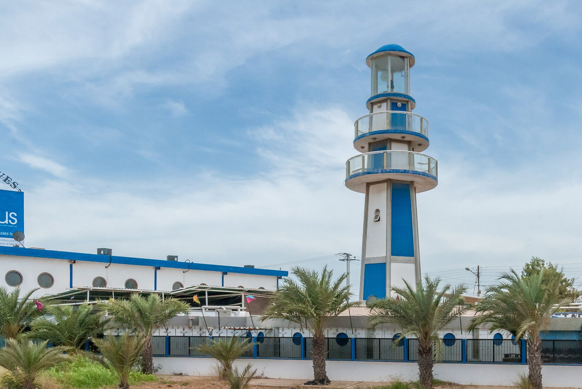 Alt text: Modern lighthouse with blue accents, surrounded by palm trees, offering scenic coastal views.