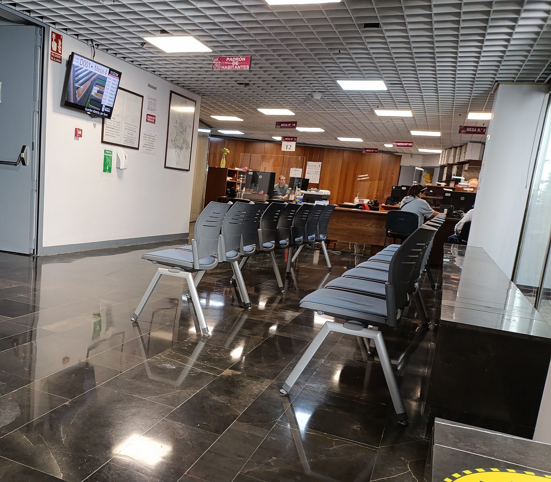Waiting area with rows of chairs, TV, and reception desk in a modern office.
