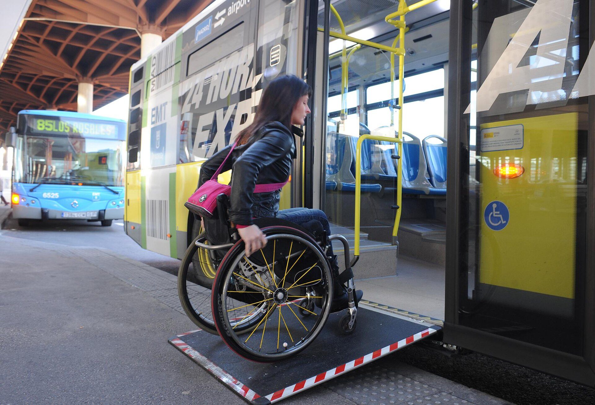 A woman in a wheelchair boarding a yellow and green bus at a bus stop.