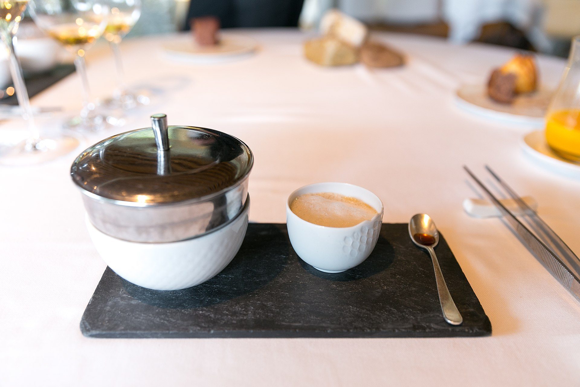 A cozy dining table with a coffee cup, teapot, and cutlery on a black slate tray.