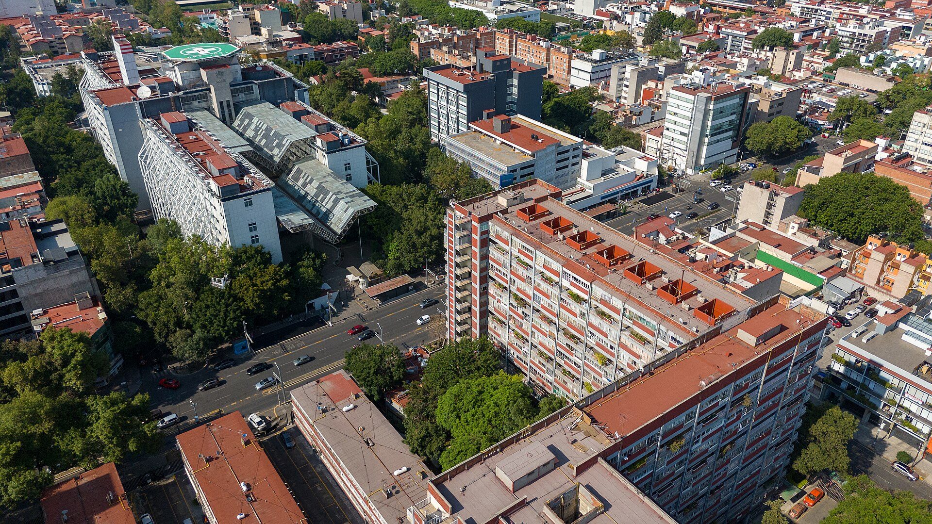 Aerial view of a city with modern buildings, greenery, and a busy street.