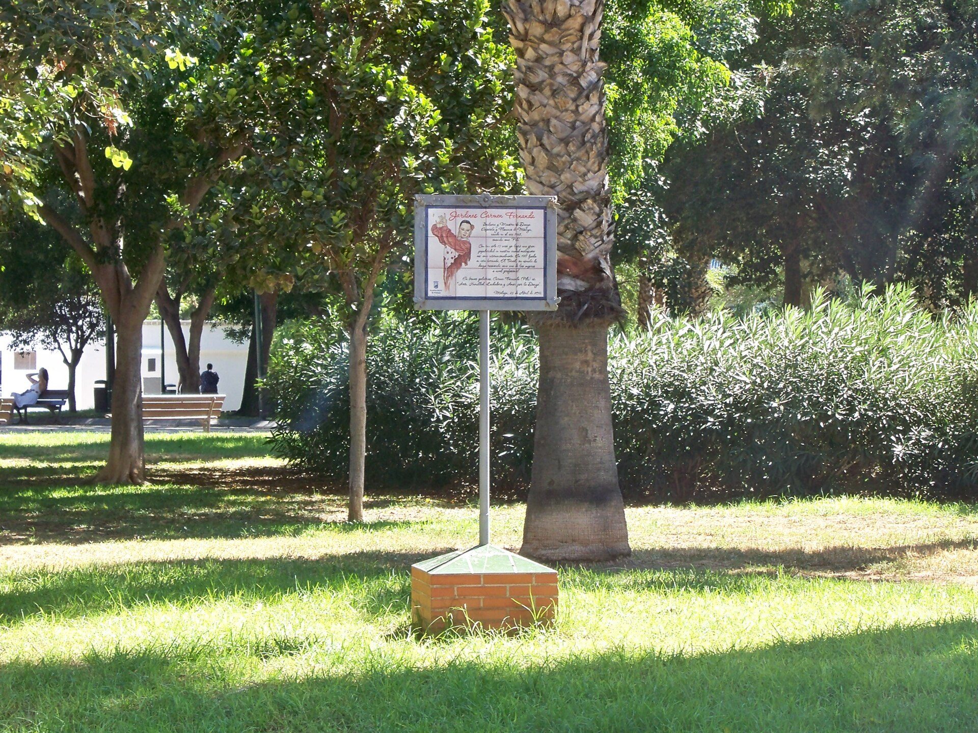 A park with a sign, trees, and a bench in the background.