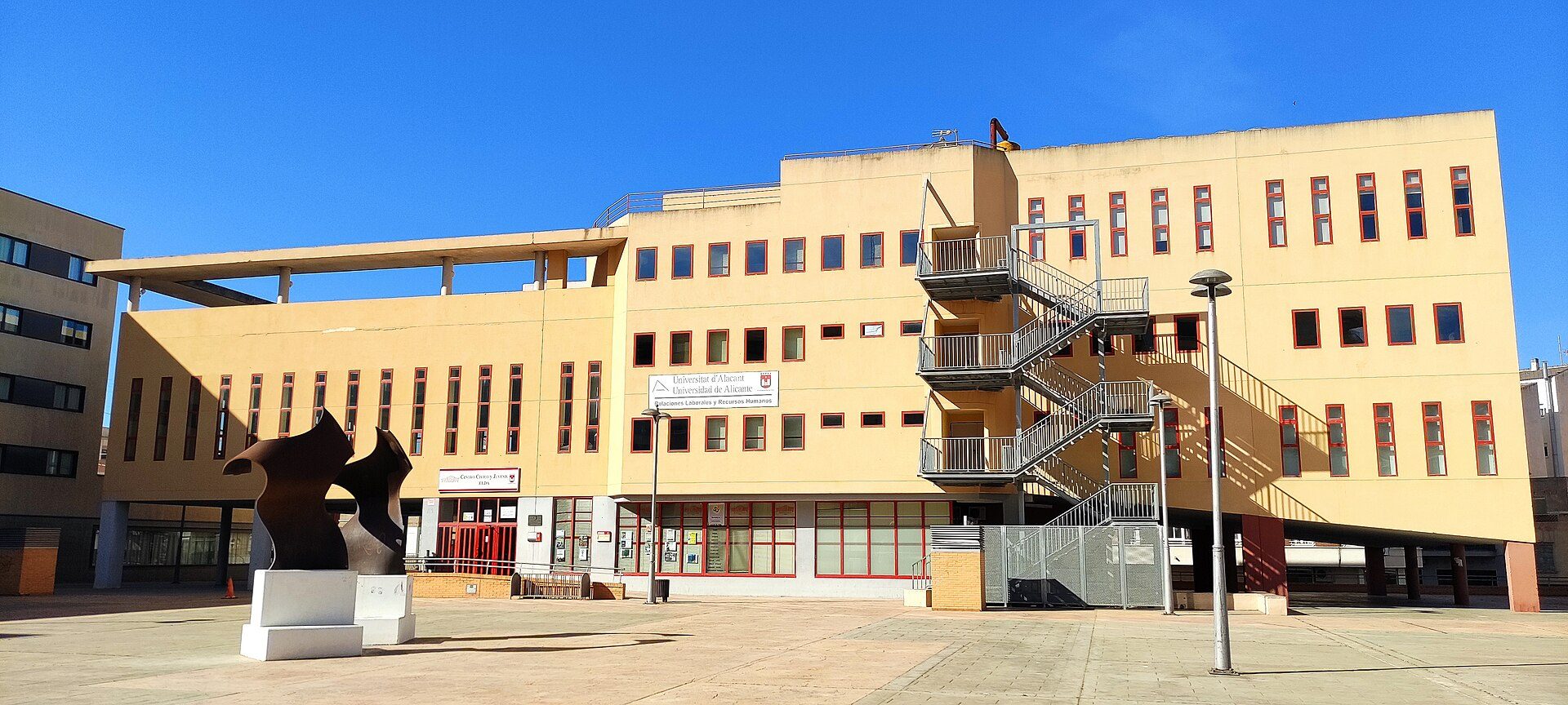 Modern building with large windows, outdoor staircase, and a sculpture in the courtyard.