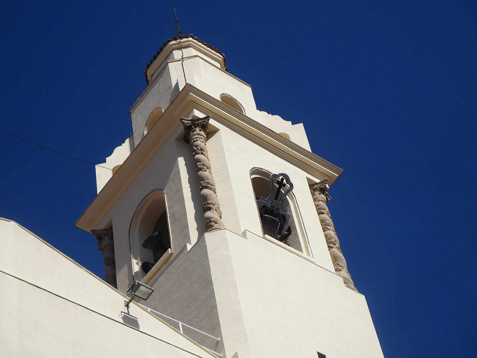 Alt text: White bell tower with arched windows and a clear blue sky background.