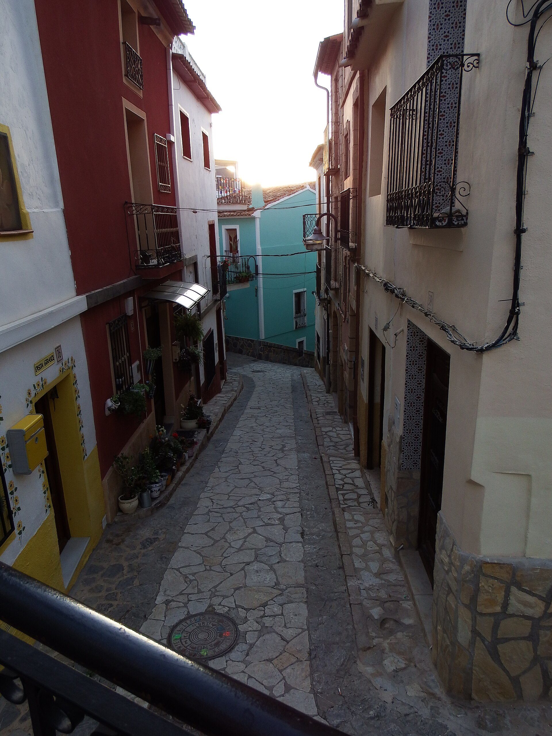 Cozy courtyard with stone flooring, surrounded by colorful buildings, featuring balconies and plants.