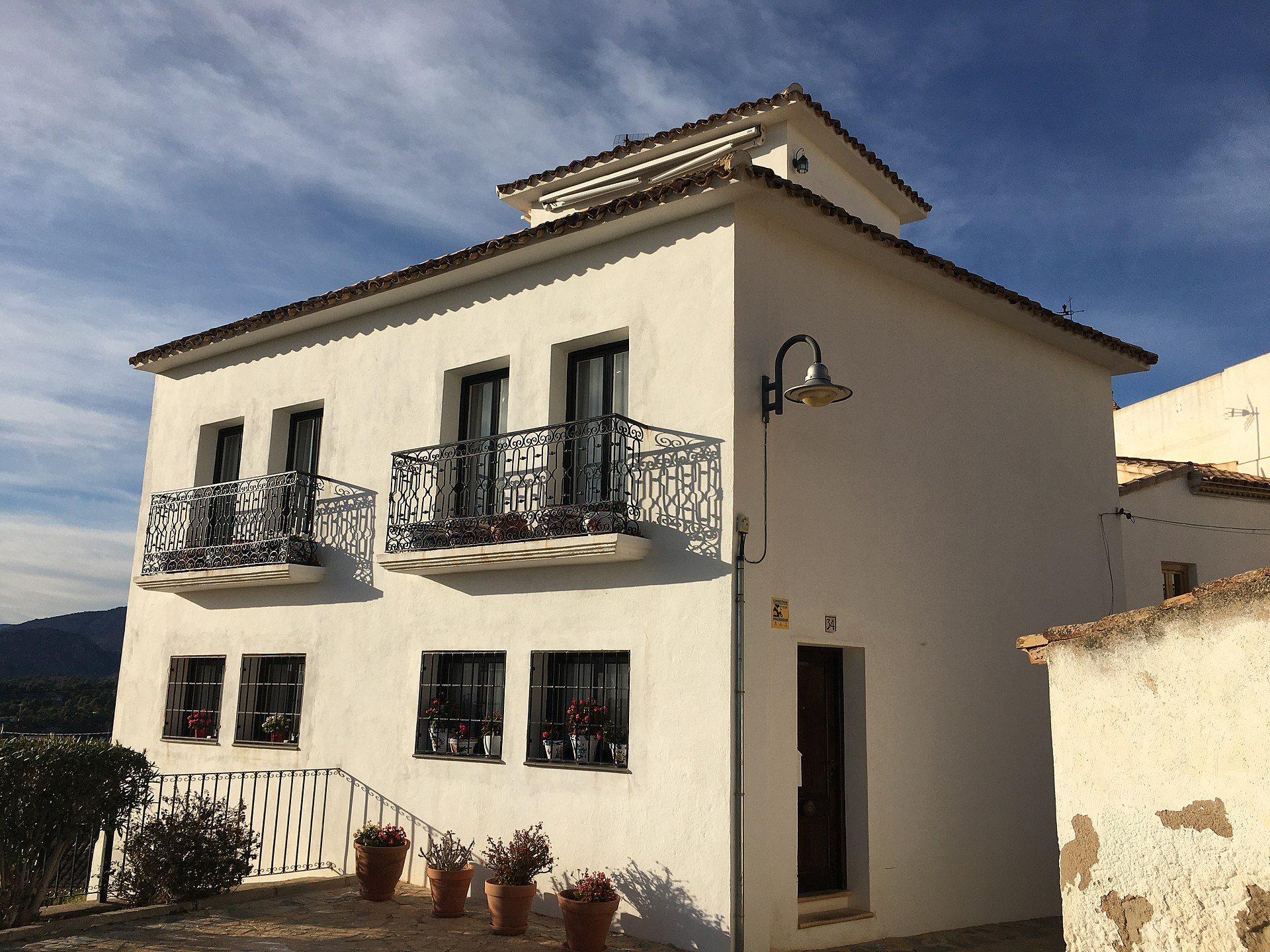 Two-story white house with balconies, mountain view, potted plants, and a street lamp.