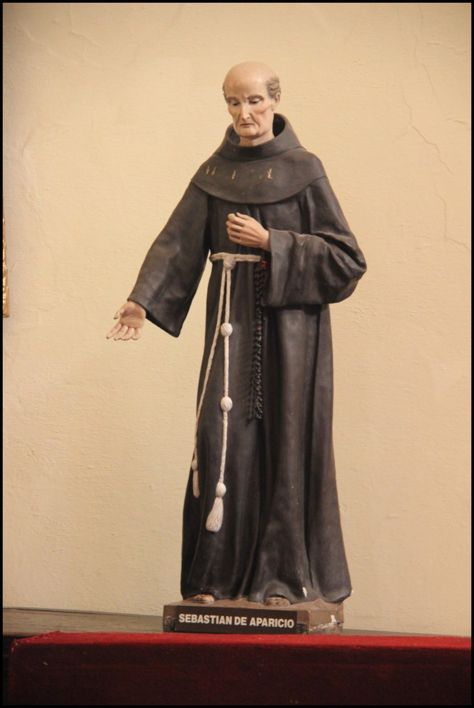 A statue of a robed figure with a rosary, standing on a pedestal.
