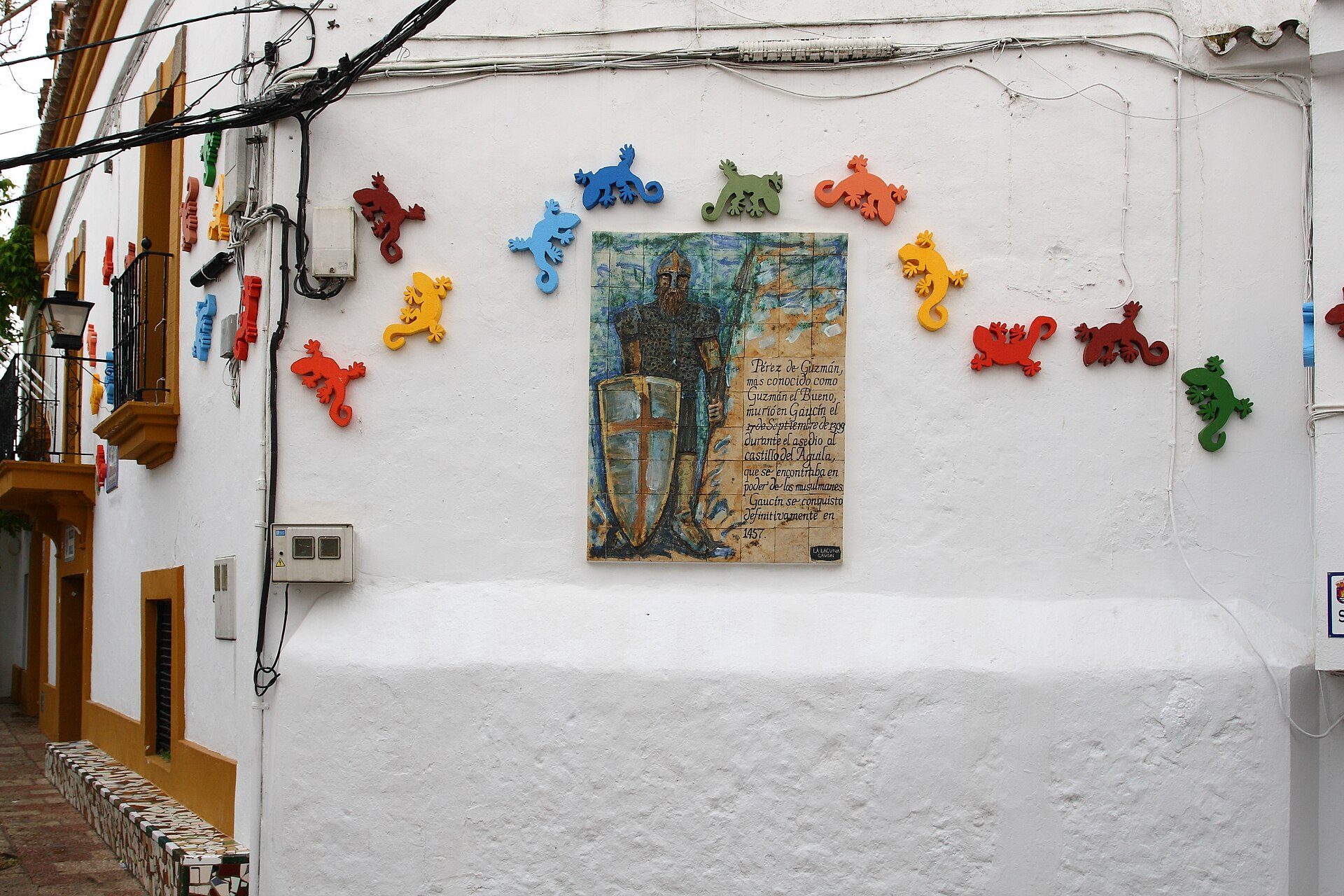 White wall with colorful bear sculptures, framed painting, and electrical wires.