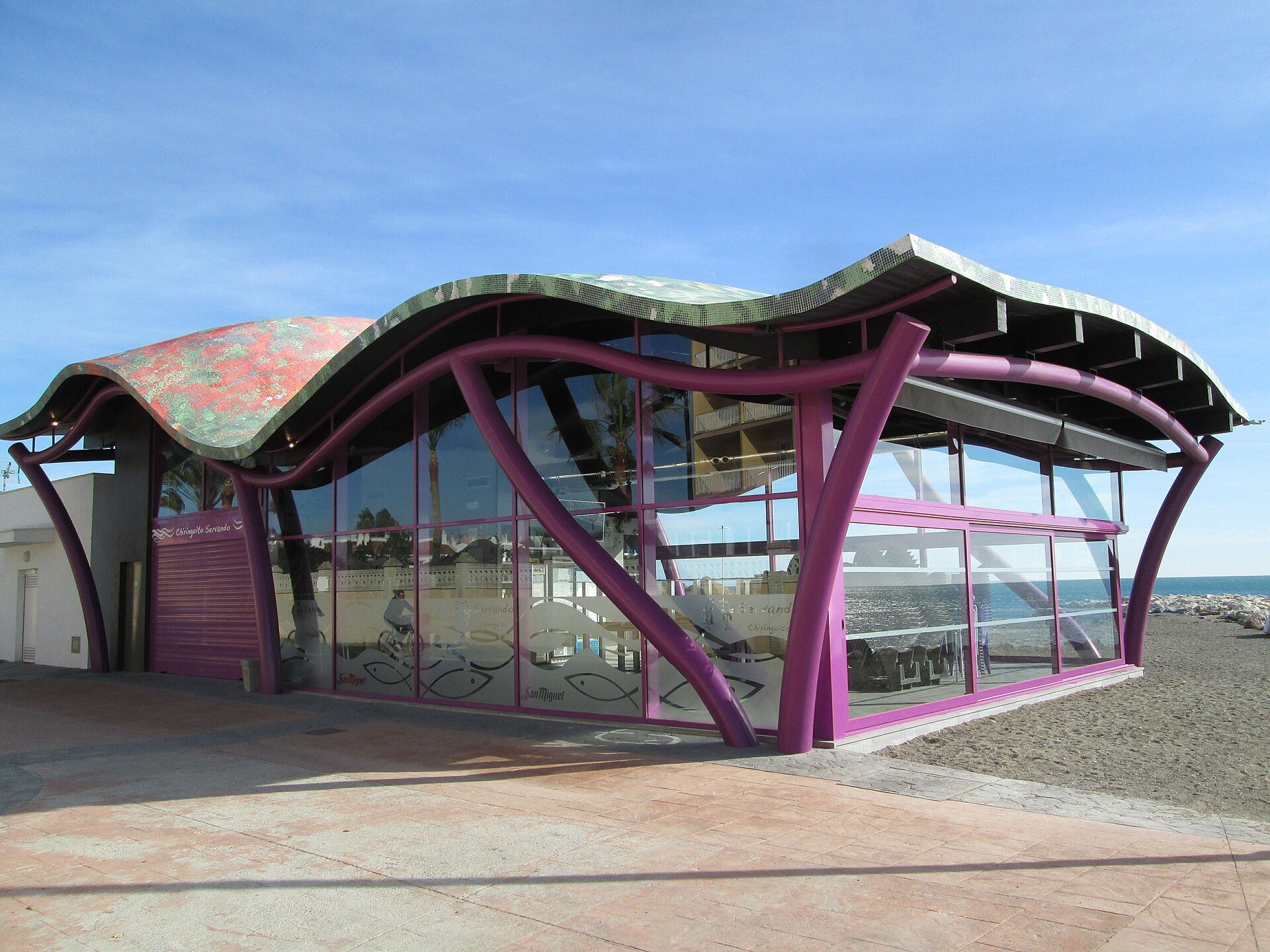 Modern beachfront building with large glass windows and vibrant purple accents.