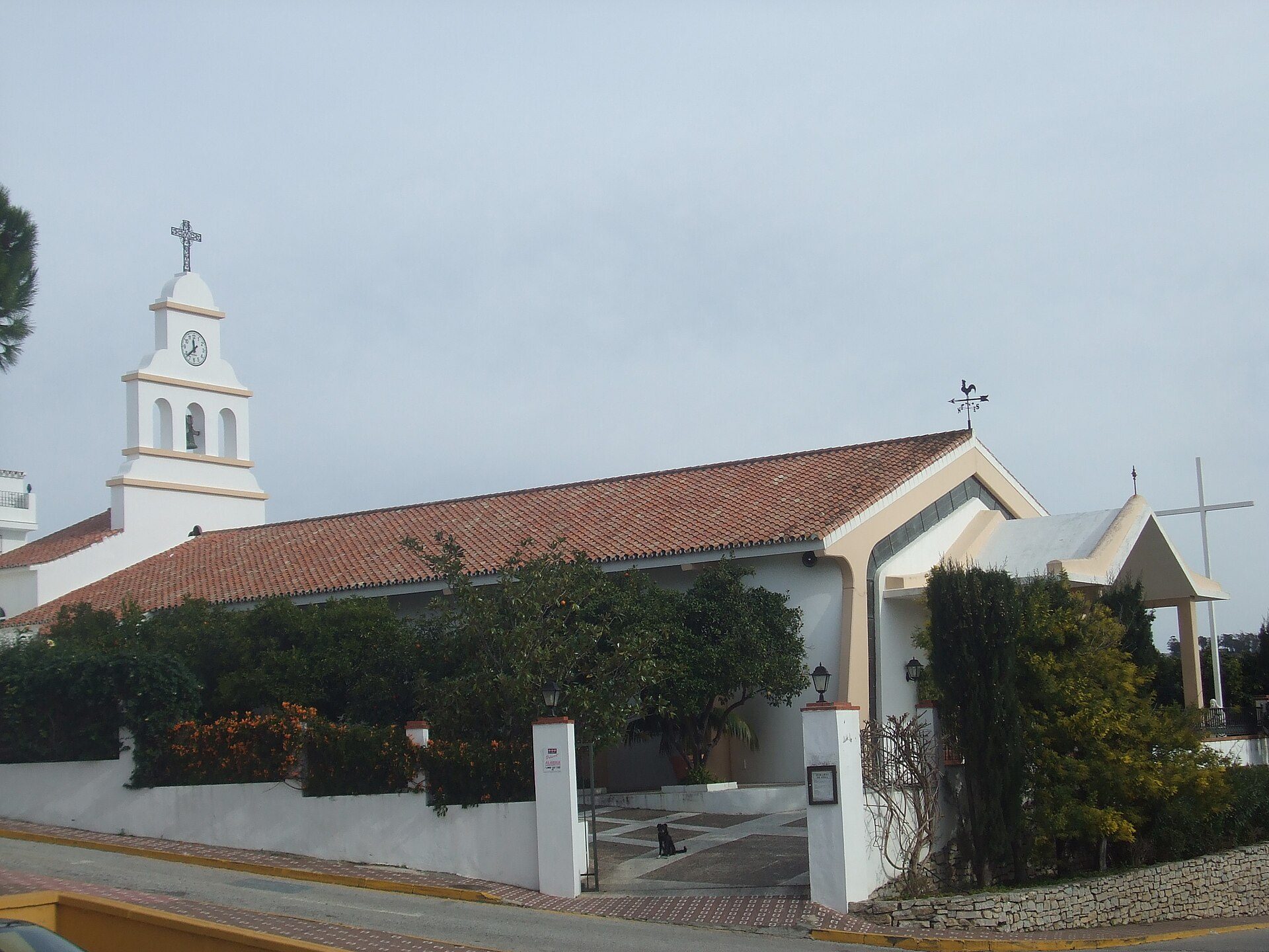 A quaint church with a red-tiled roof, white walls, and a clock tower.