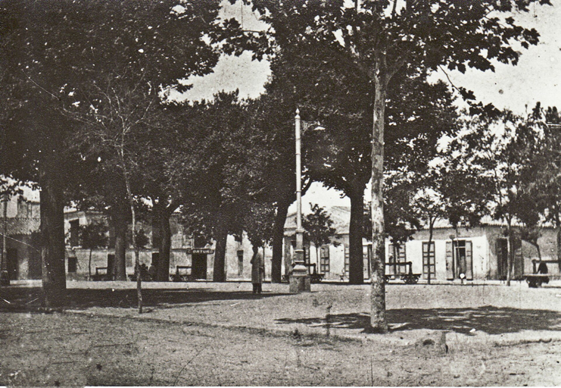 A black and white photo of a park with trees and a building in the background.