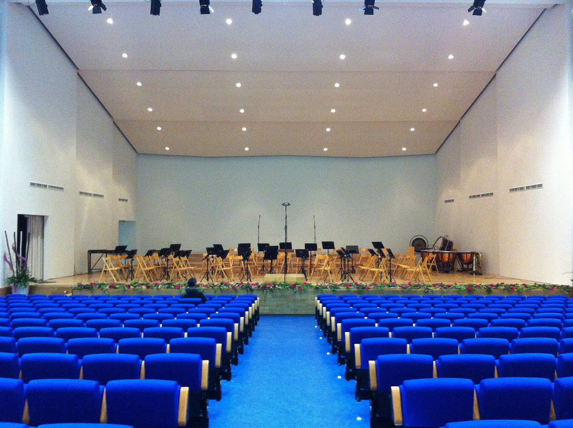 Alt text: Interior view of a spacious auditorium with blue seats and a stage.