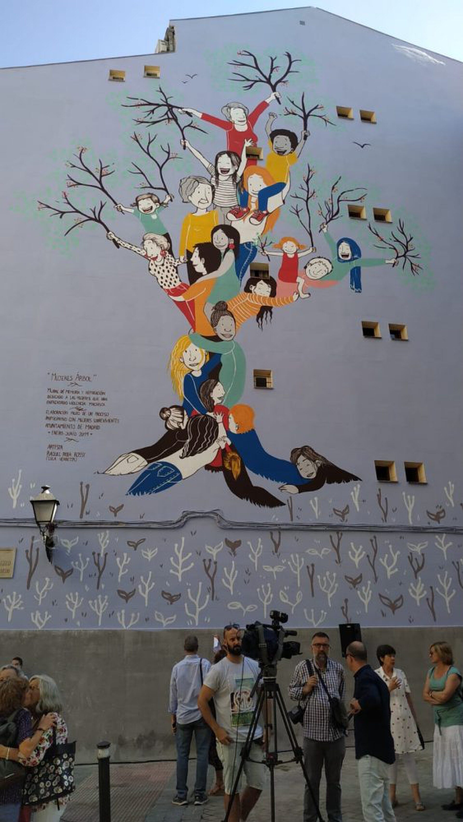 Mural of people and birds on a building wall, with people gathered below.