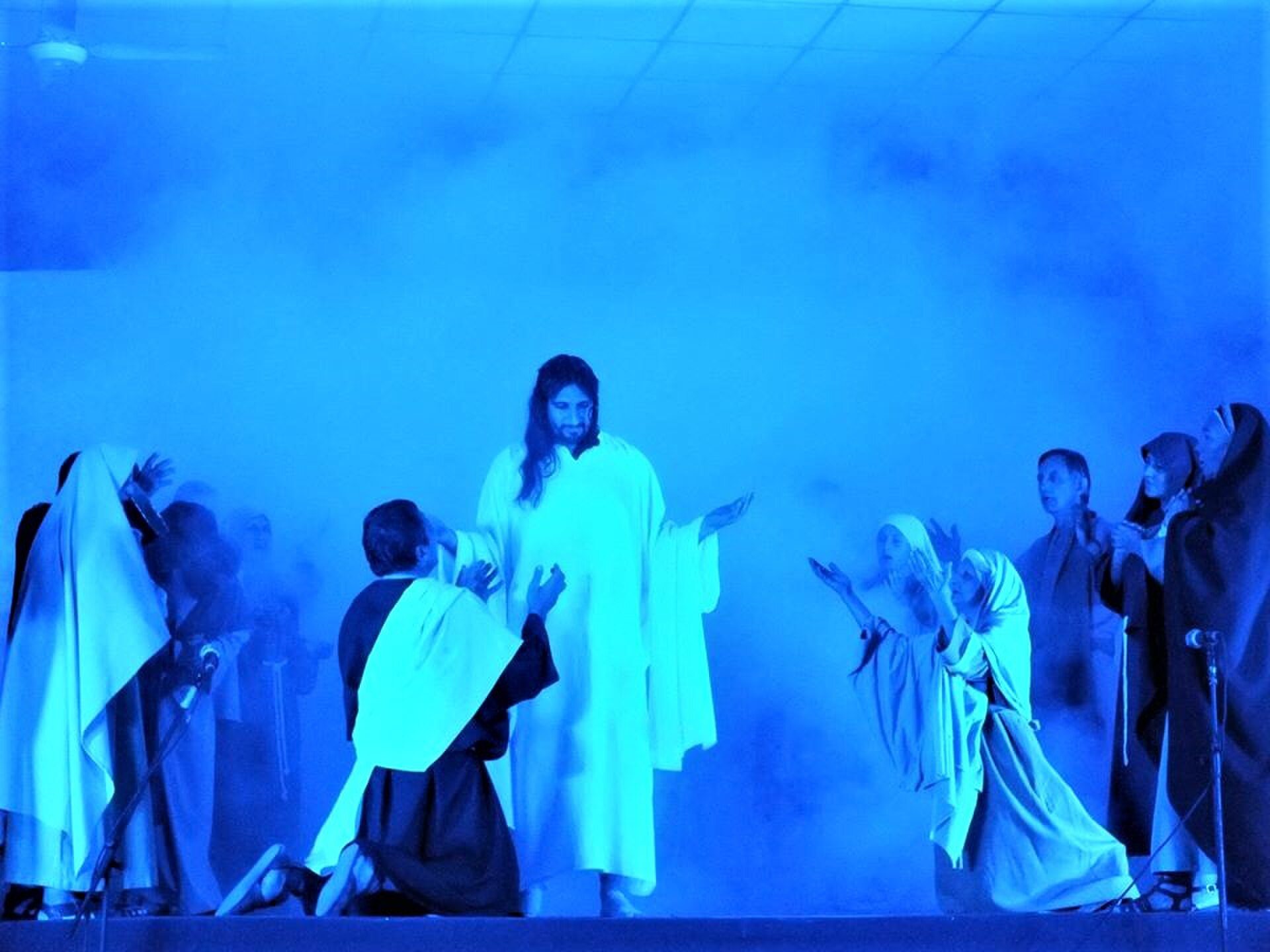 A theatrical stage performance with blue lighting, featuring actors in robes.