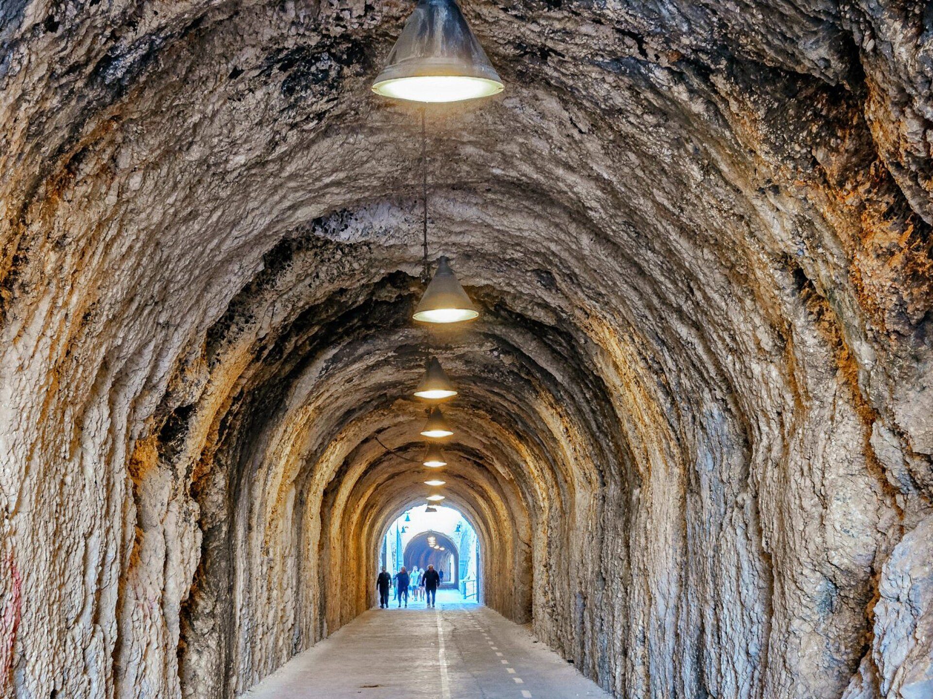 A stone tunnel with hanging lights, leading to an open doorway.