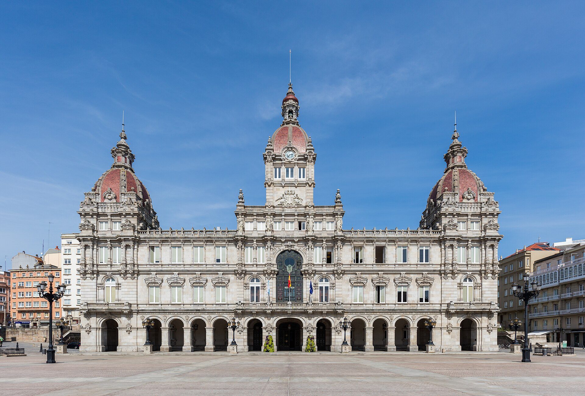 Alt text: Historic building with clock tower, red domes, and arched entrance, set against a clear blue sky.