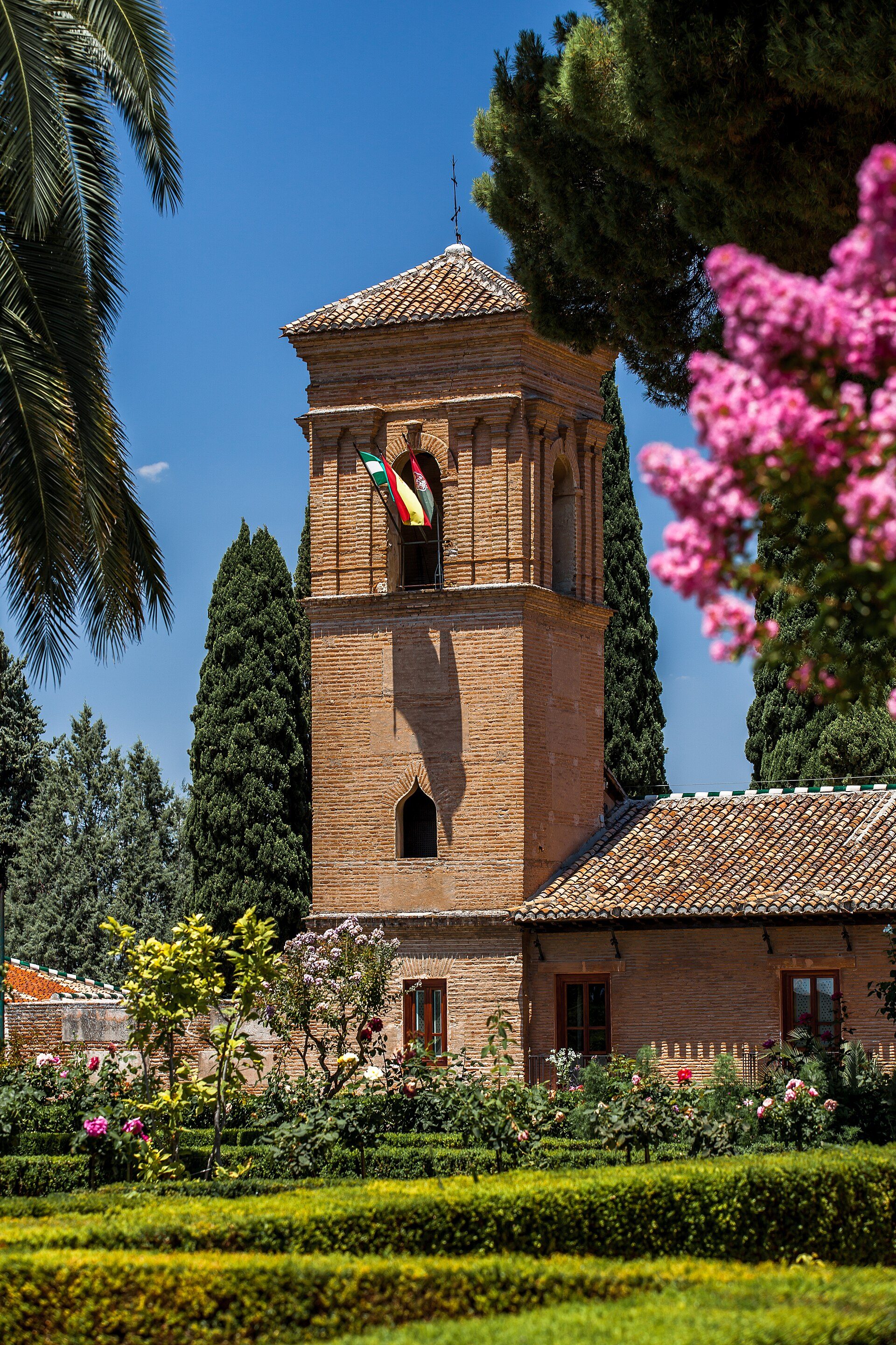 Traditional tower with garden view, featuring arched windows and a flag.