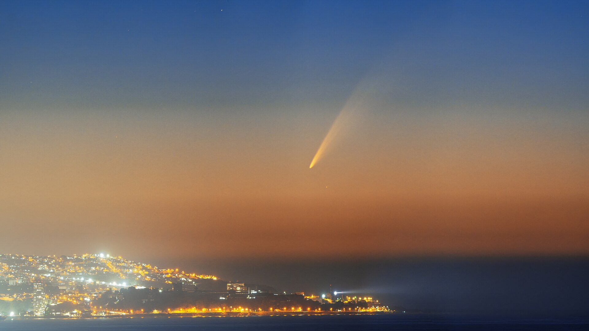 Alt text: Evening cityscape view from room with bright lights and a clear sky.
