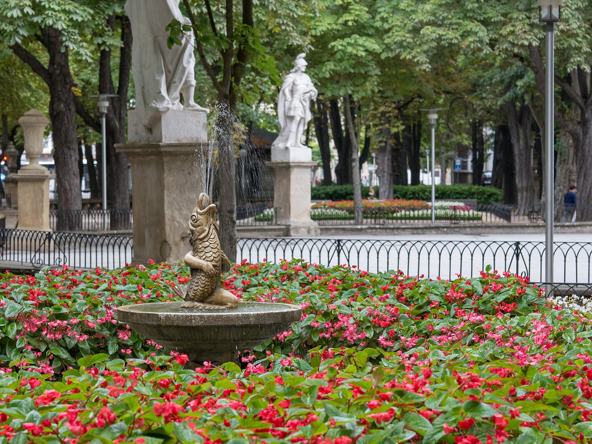 Alt text: Outdoor fountain surrounded by vibrant red flowers and greenery.