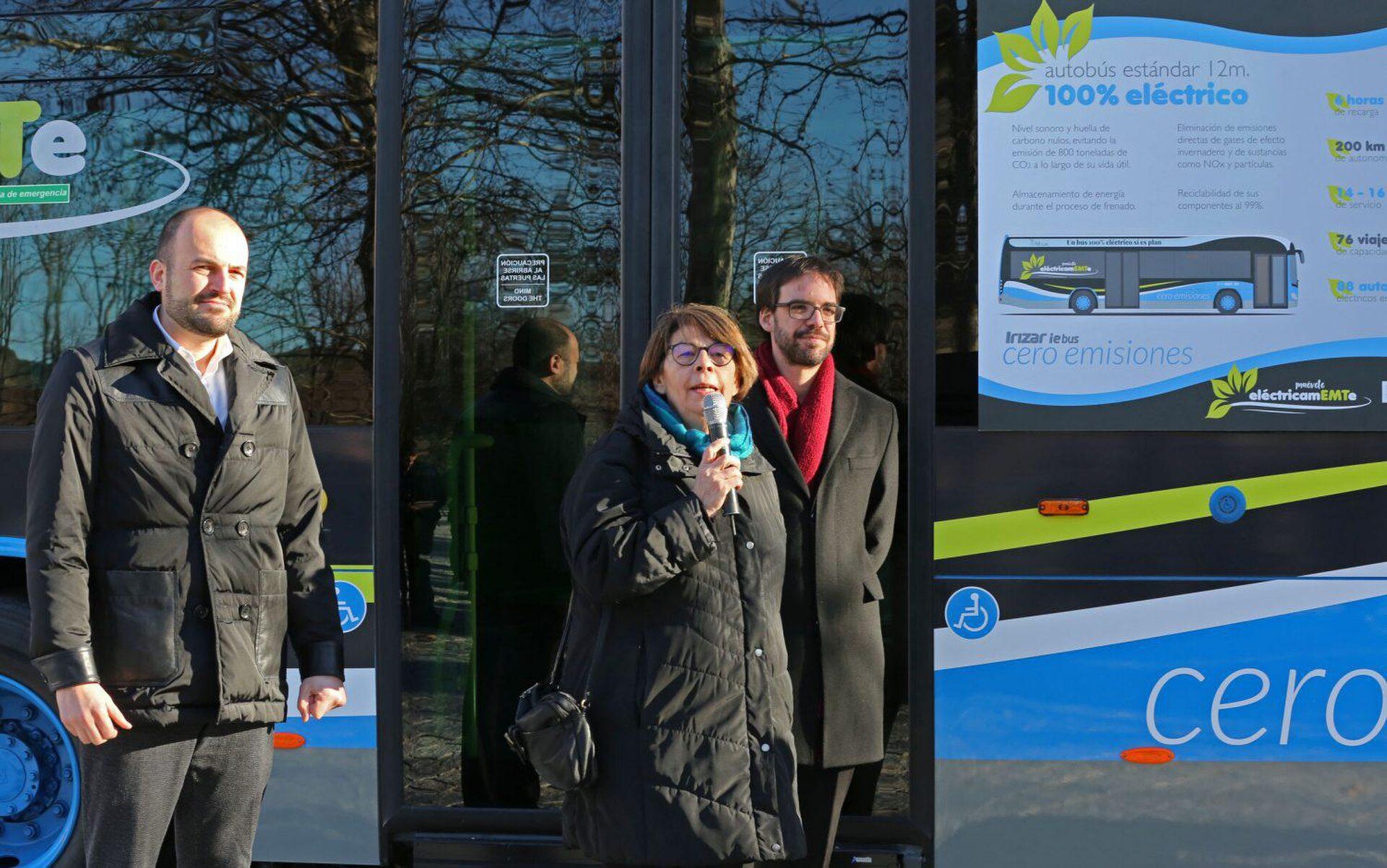 Three people standing in front of a bus with an electric bus advertisement.