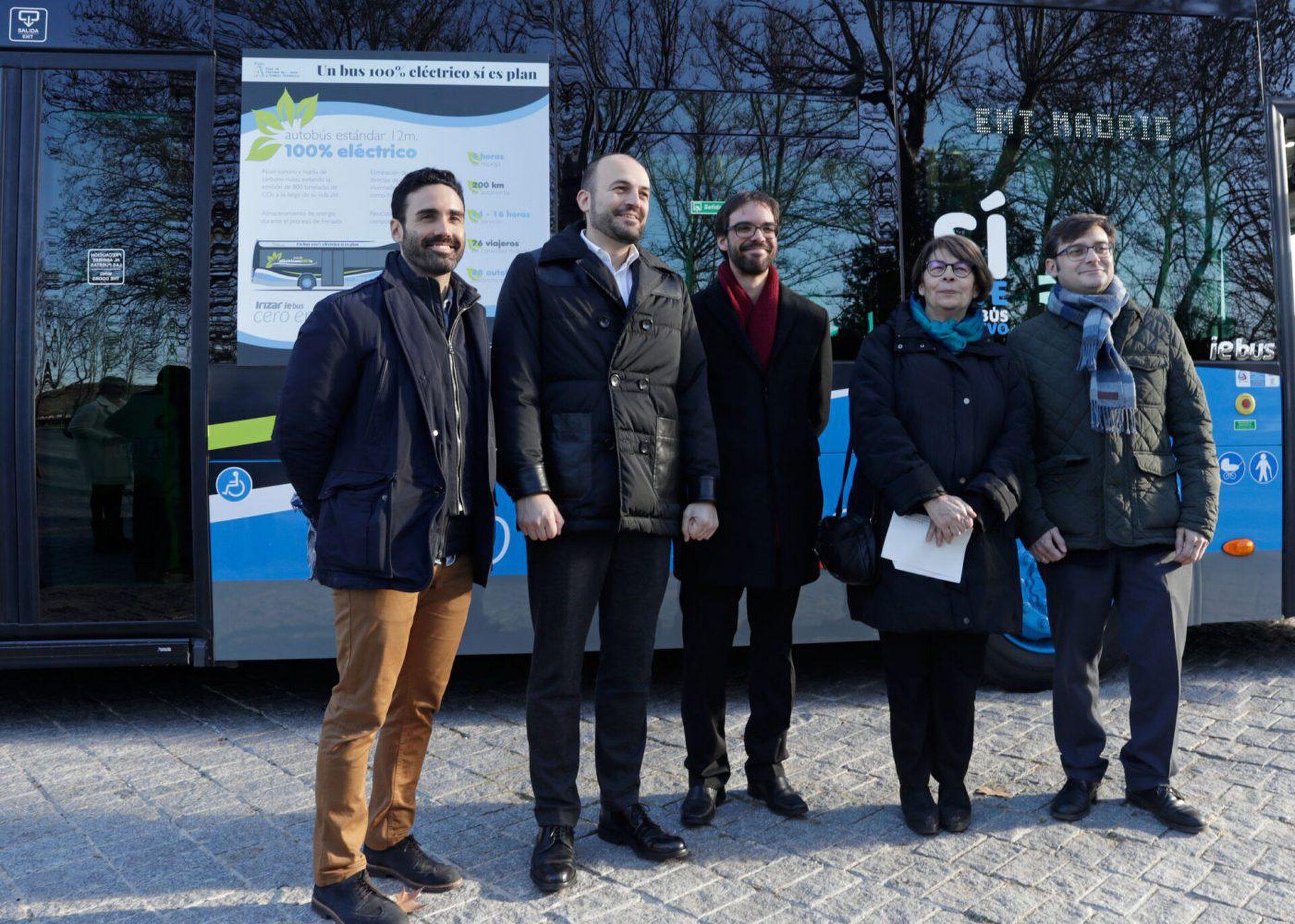 Five people standing in front of a bus with a 100% electric vehicle advertisement.