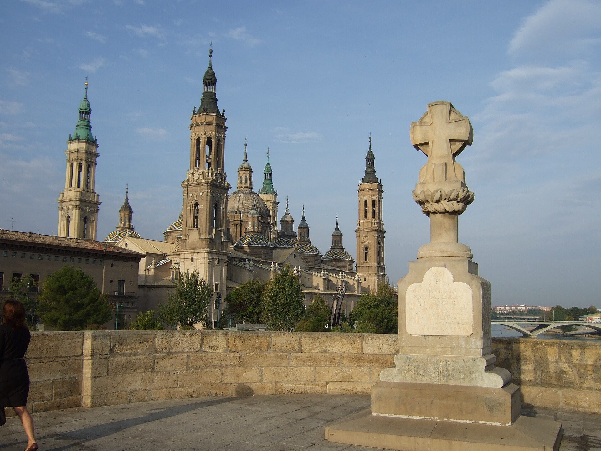Alt text: Historic church with twin towers and dome, cross monument, stone wall, and trees.