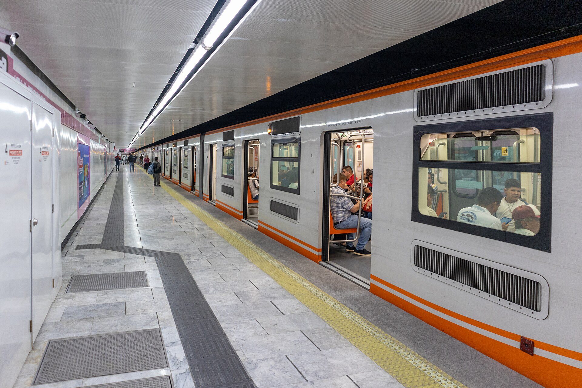 Subway platform with a train, passengers, and tiled walls.