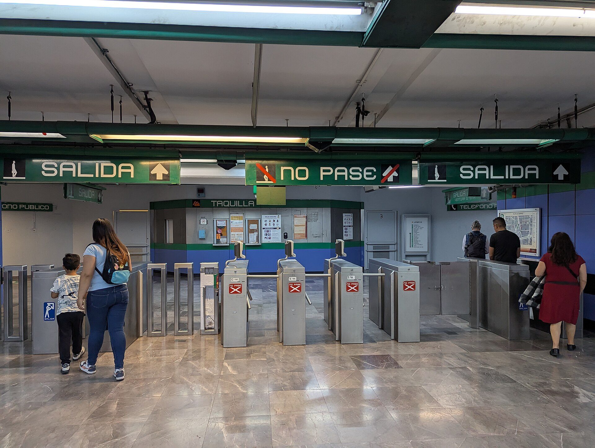 Subway station with turnstiles, signs, and people waiting.