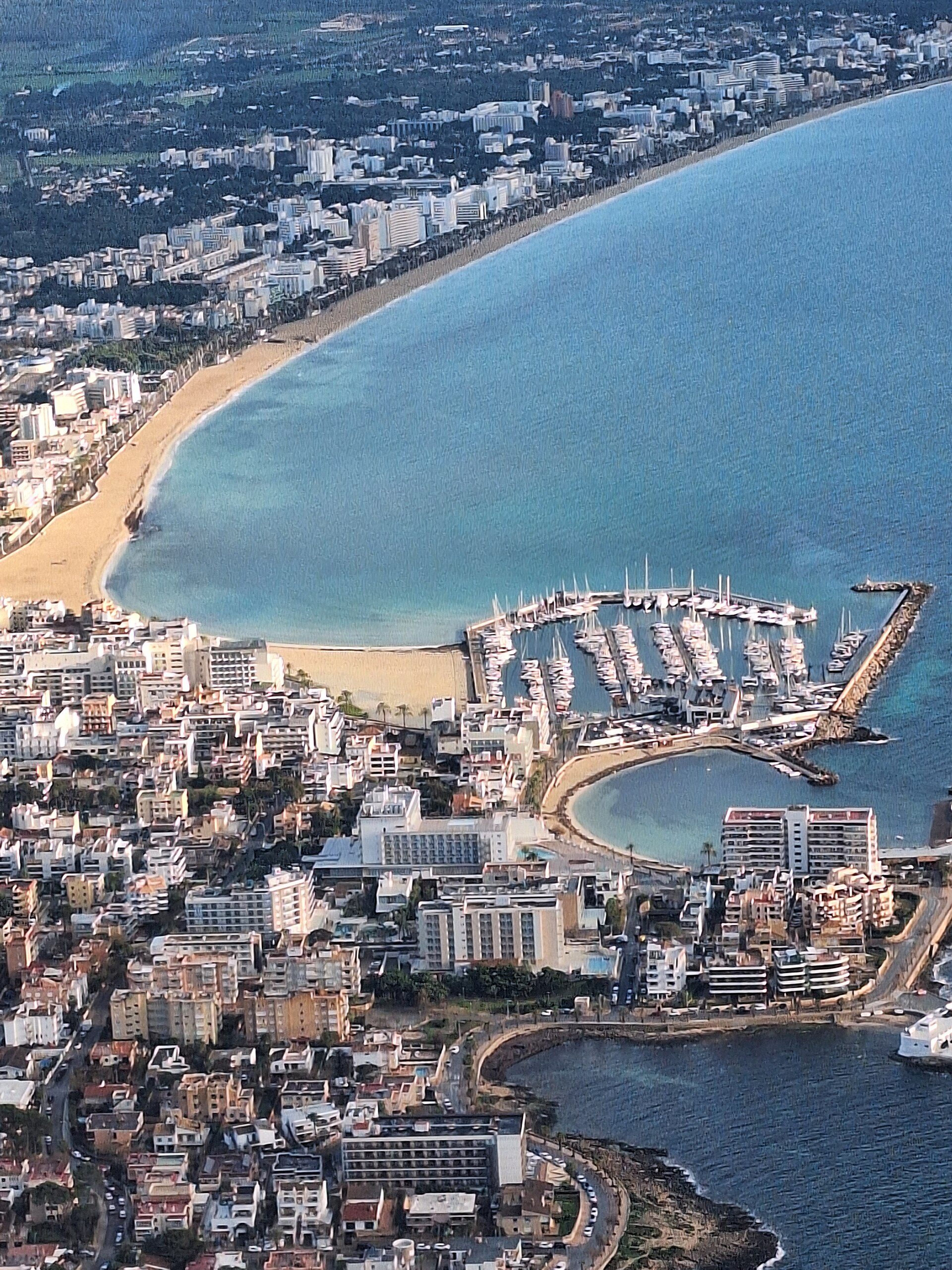 Aerial view of a coastal city with a marina and sandy beach.