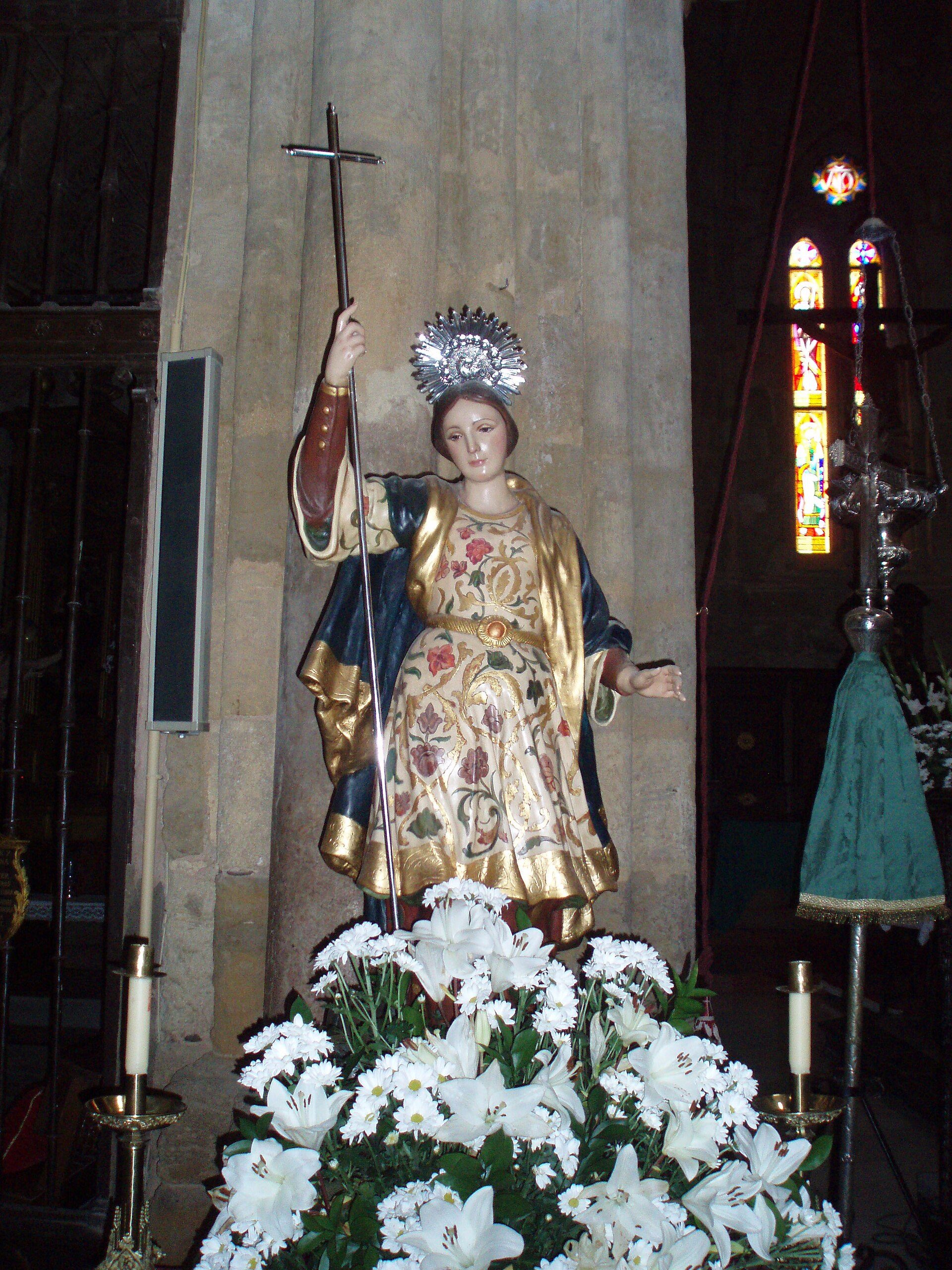 Alt text: A statue of a robed figure holding a cross, surrounded by white flowers, in a church setting.