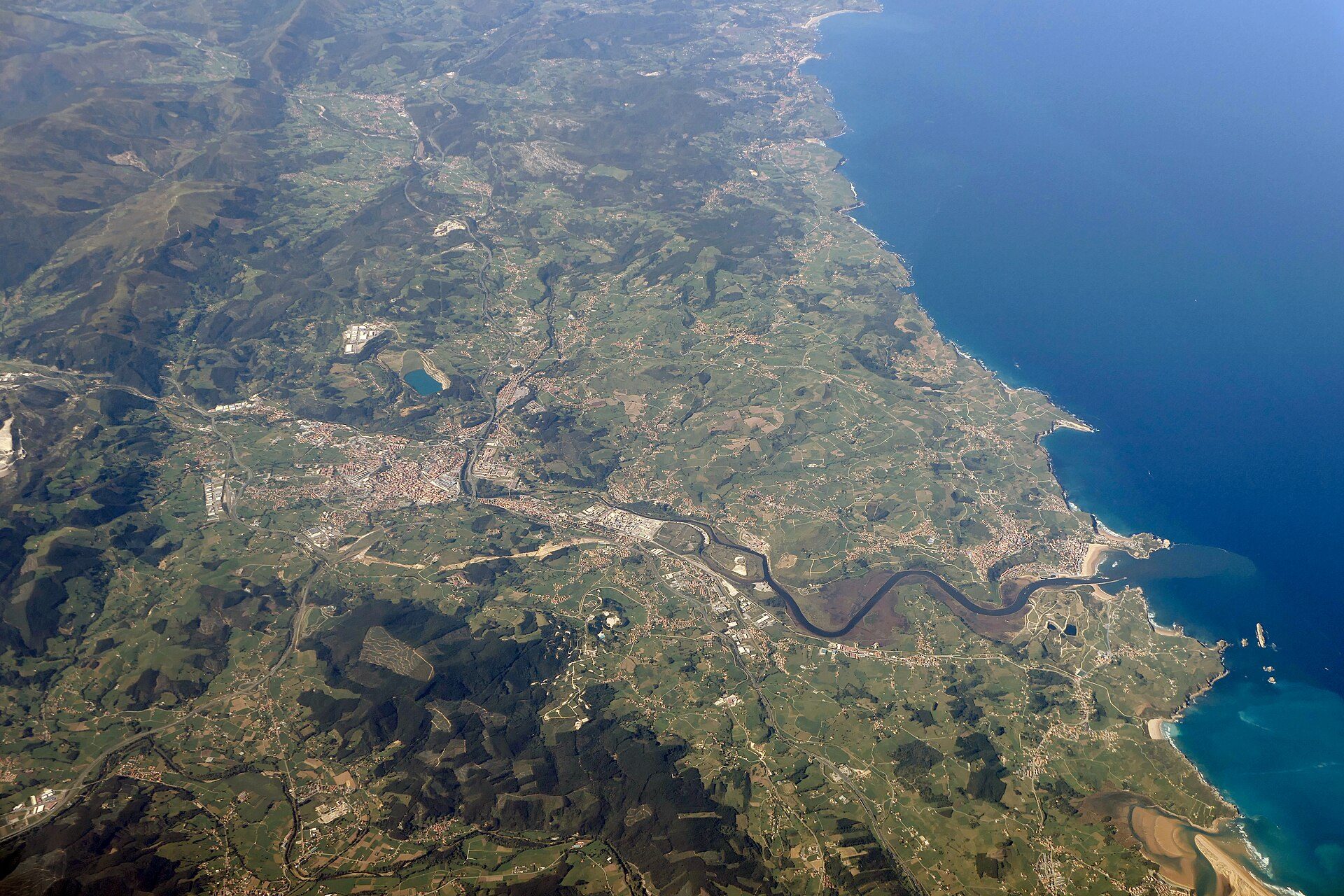Aerial view of a coastal town with a river, greenery, and the sea.